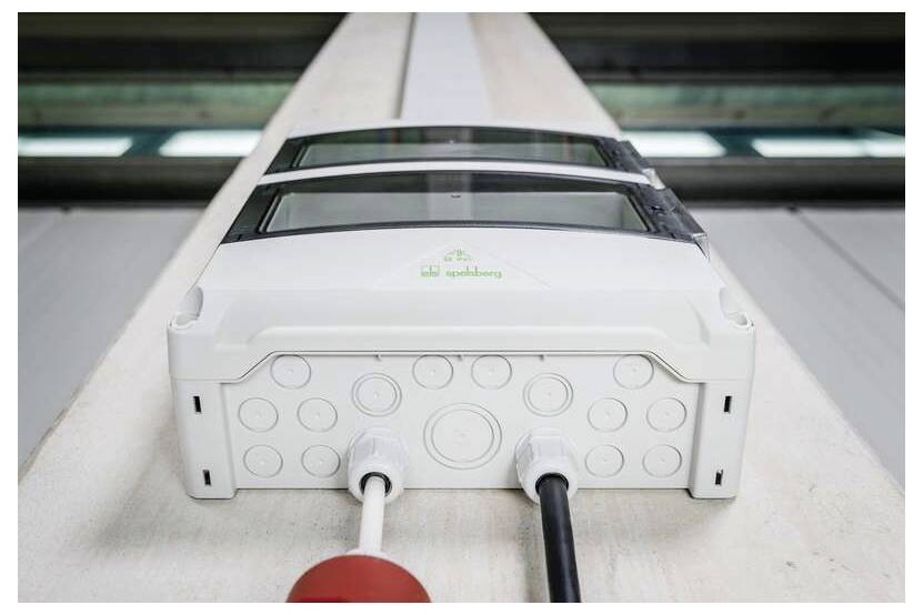 Weißer Elektrostecker mit mehreren kreisförmigen Anschlüssen und zwei angeschlossenen Kabeln auf einem Förderband oder einer Produktionslinie