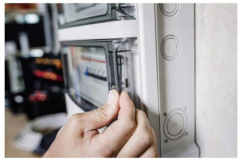Eine Hand öffnet eine Elektroschaltafeltür, um auf Leistungsschalter in einer an der Wand montierten Box zuzugreifen.