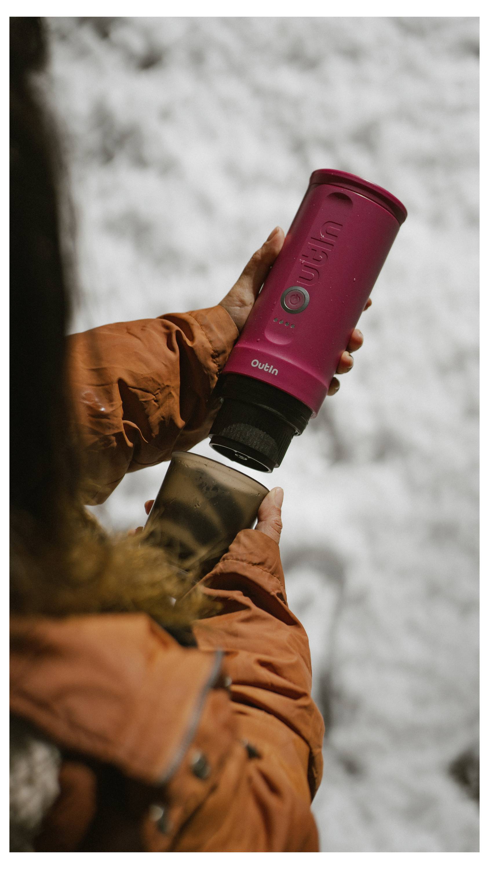 Eine Person in einer braunen Jacke hält eine rote Reisestasse über einem verschneiten Hintergrund und zeigt eine Außenumgebung mit Fokus auf das Design der Tasse.