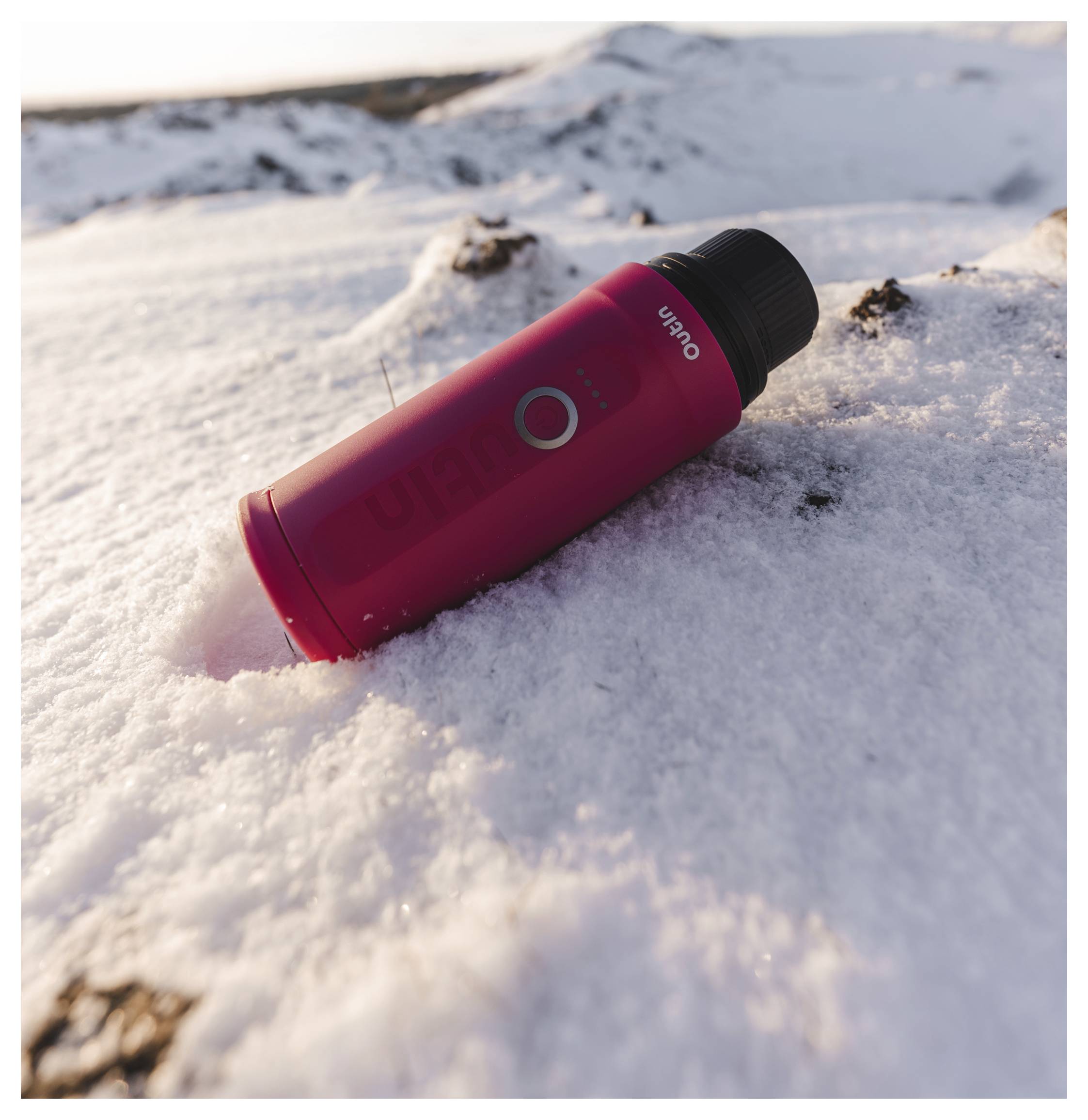 Eine rote isolierte Flasche liegt auf verschneitem Gelände mit einer Berglandschaft im Hintergrund.