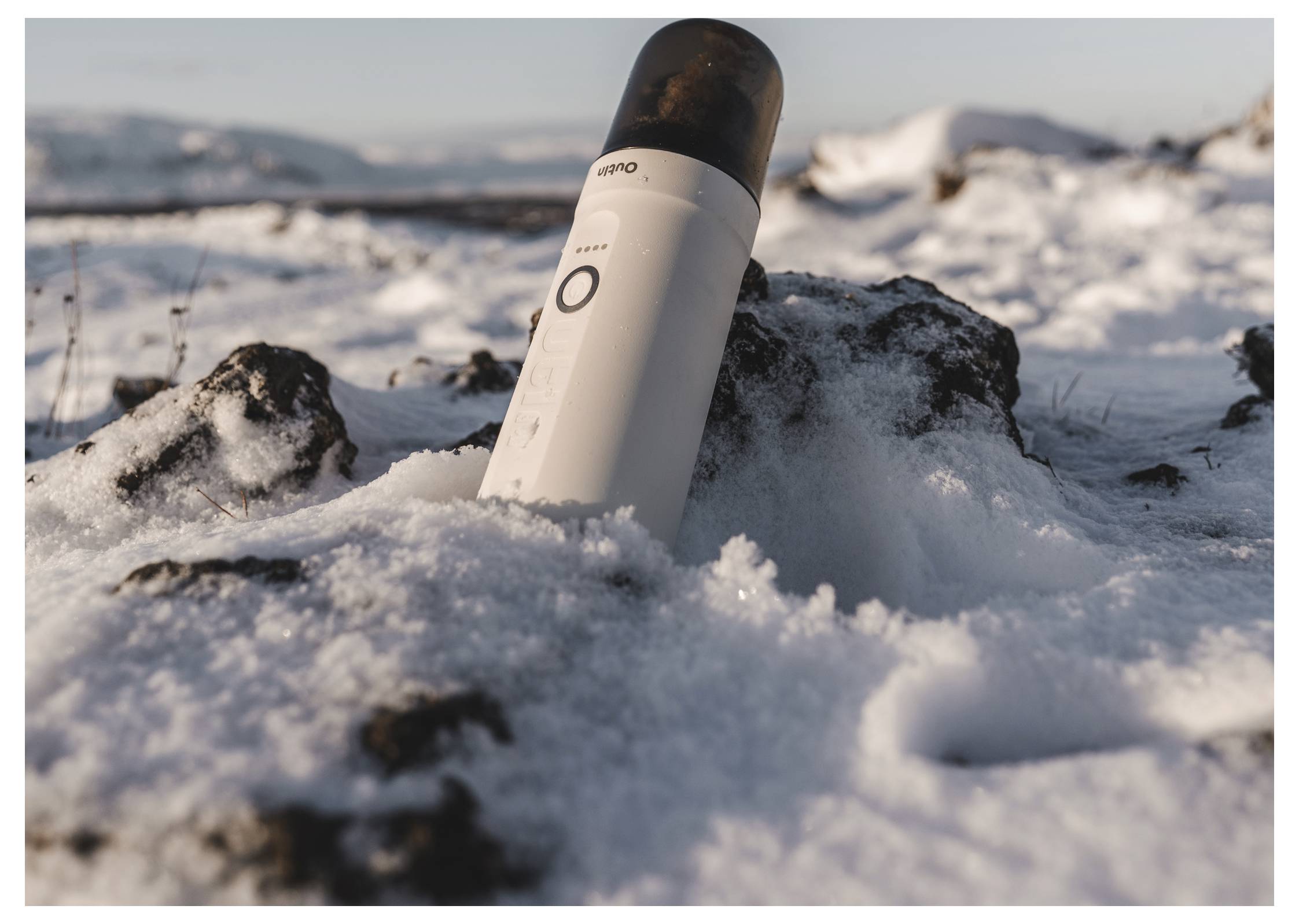 Eine aufrecht stehende Flasche auf schneebedeckten Steinen mit einer bergigen Landschaft im Hintergrund.