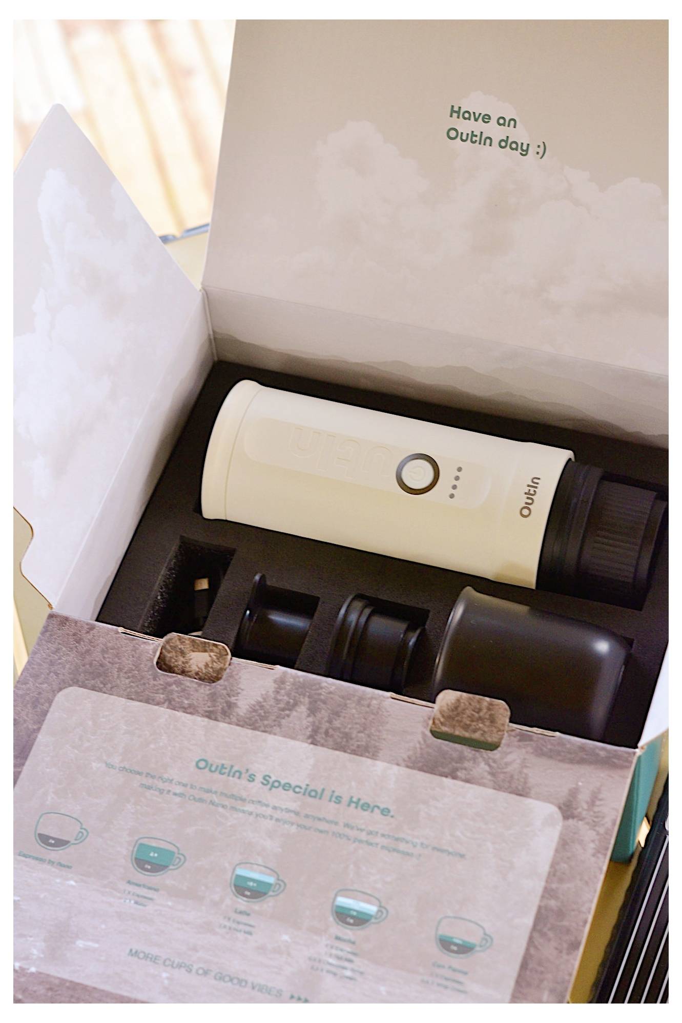 Ein weißer tragbarer Behälter und zwei schwarze Deckel in einer offenen Pappschachtel. Auf dem Deckel der Schachtel steht „Have an Outlin day :)