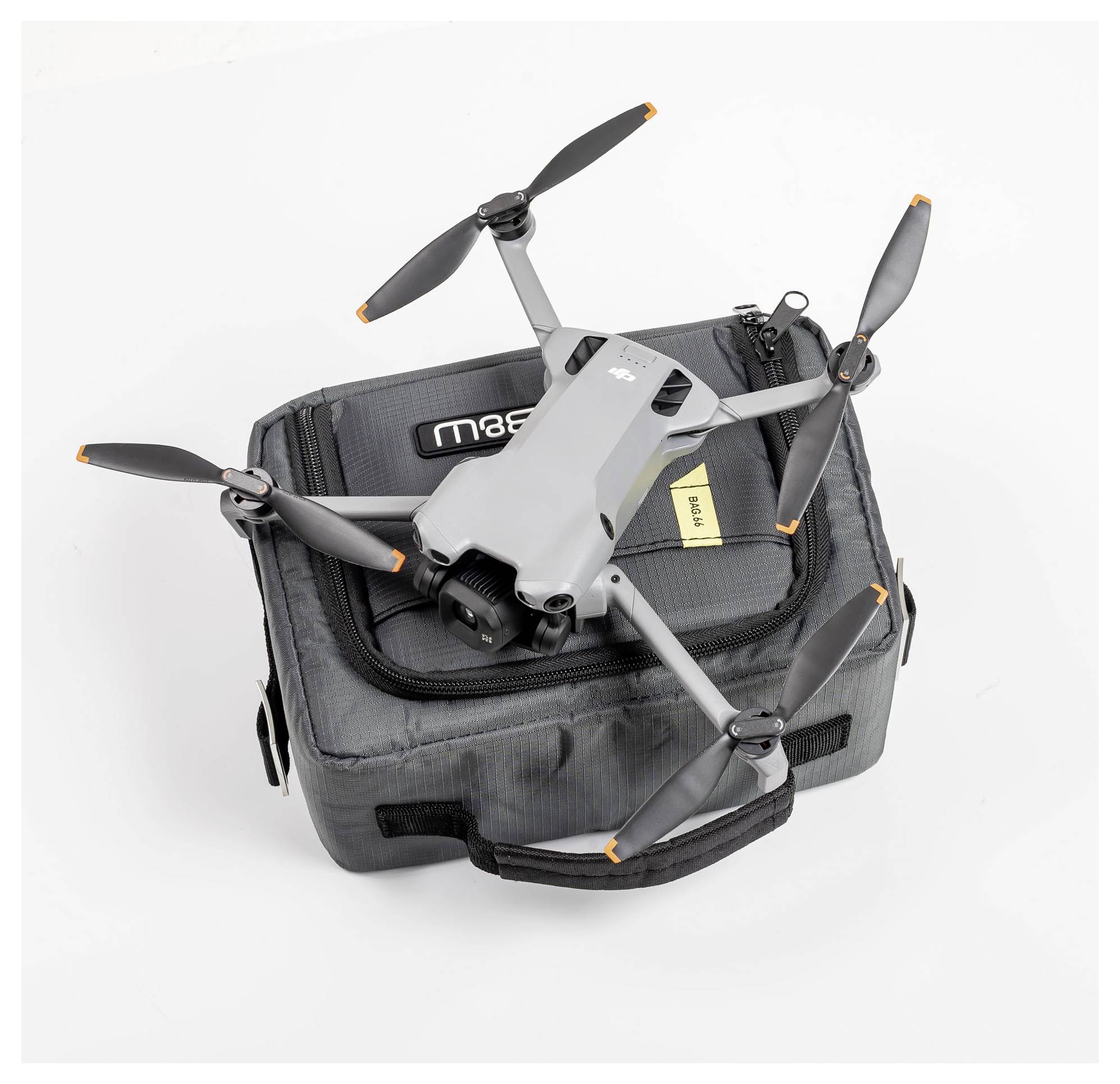 Eine kompakte, graue Drohne mit vier Propellern ruht auf einem grauen Tragekoffer. Der Koffer hat einen schwarzen Griff und ein sichtbares Etikett.