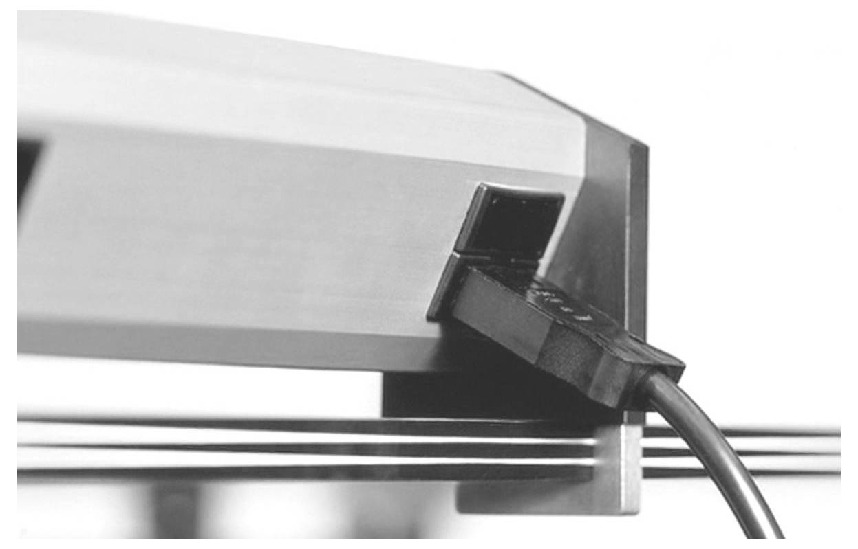 Eine Nahaufnahme eines Metallobjekts mit einem angeschlossenen Kabel, das über drei parallelen Drähten positioniert ist. Die Umgebung scheint industriell oder mechanisch zu sein.