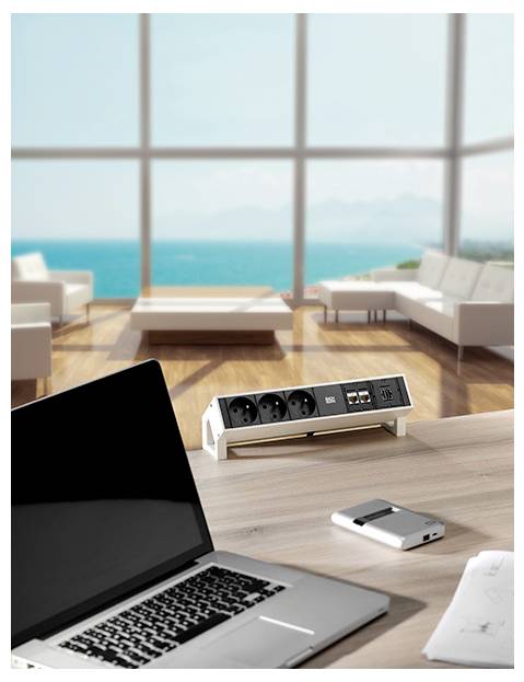 Ein modernes Büro mit einem Laptop und einem Stromverteiler auf einem Holzschreibtisch. Große Fenster geben den Blick auf ein malerisches Meerespanorama und zeitgenössische Möbel frei.