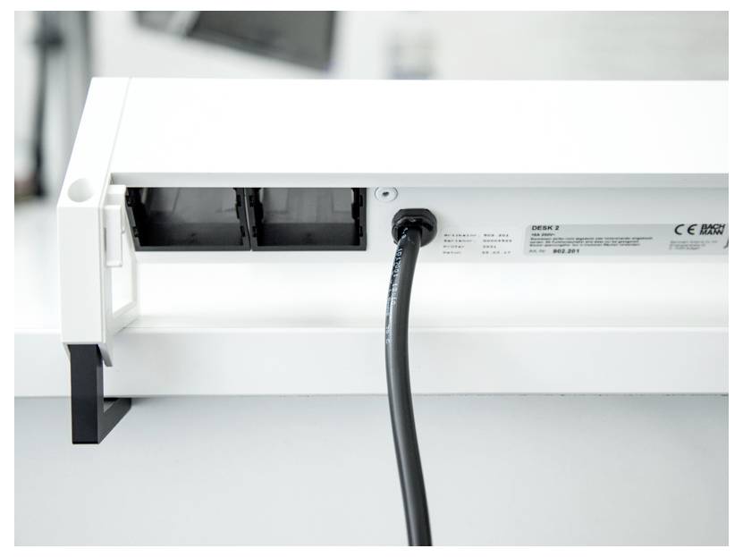 Eine Nahaufnahme eines Schreibtisch-Kabelorganisationssystems mit Steckdosen und einem angesteckten schwarzen Kabel, das ein ordentliches und organisiertes Setup zeigt.