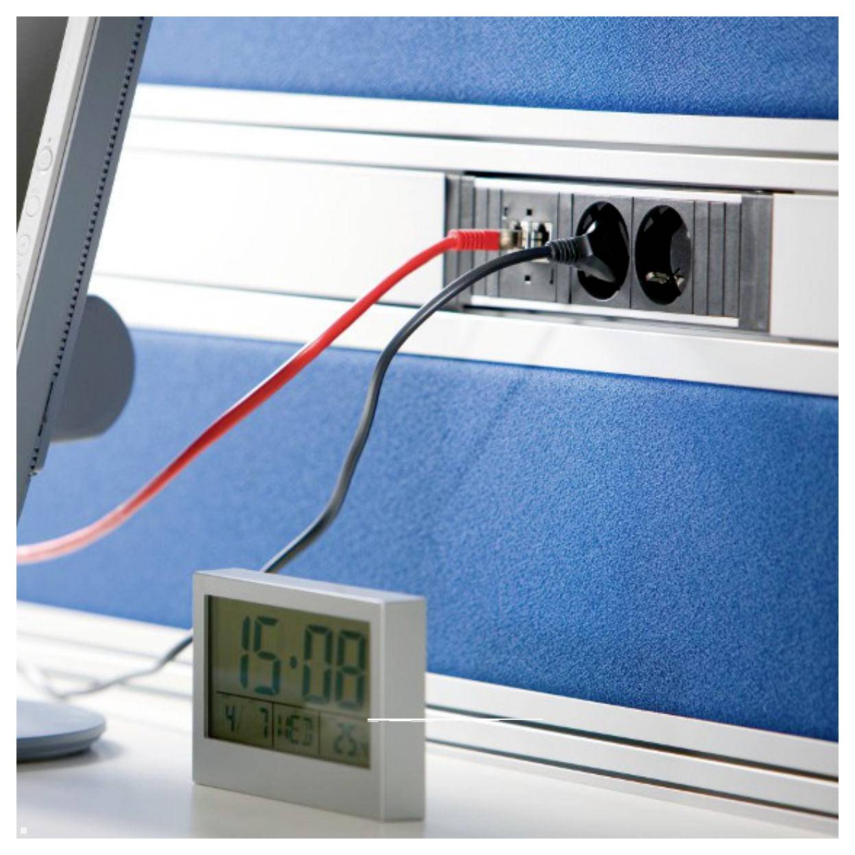 Ein Steckerleiste mit mehreren Steckdosen ist an einer Wand über einer Digitaluhr befestigt, auf der '15:08' angezeigt wird. Kabel sind mit der Leiste verbunden.