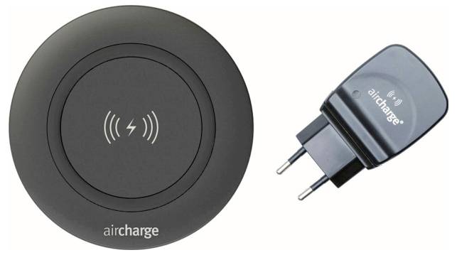 Ein großer Staubsauger auf Rädern mit einem grünen Schlauch steht im Vordergrund auf Holzböden. Eine Person steht im Hintergrund in einer Türöffnung.