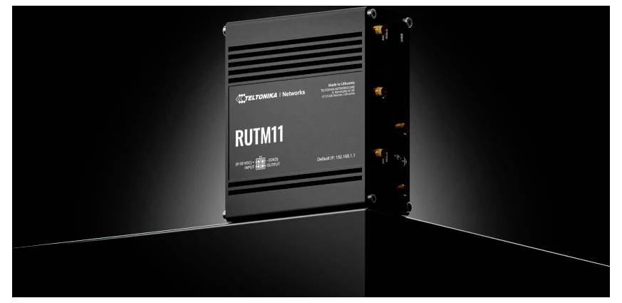 Ein schwarzer Rutronik RUTM11 Industrie-Router mit Port-Anschlüssen an der Seite, dargestellt auf einer dunklen reflektierenden Oberfläche.