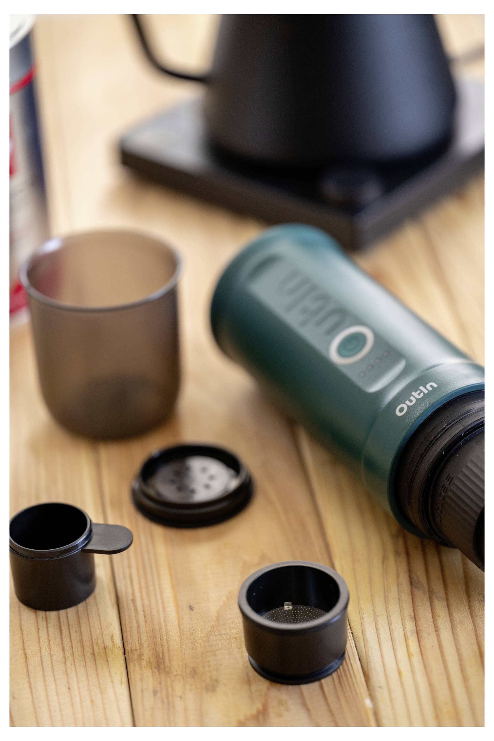 Ein tragbarer Espressokocher, der auf einem Holztisch zerlegt gezeigt wird, mit seinen Komponenten einschließlich einer Tasse und einer Filterkuppel.