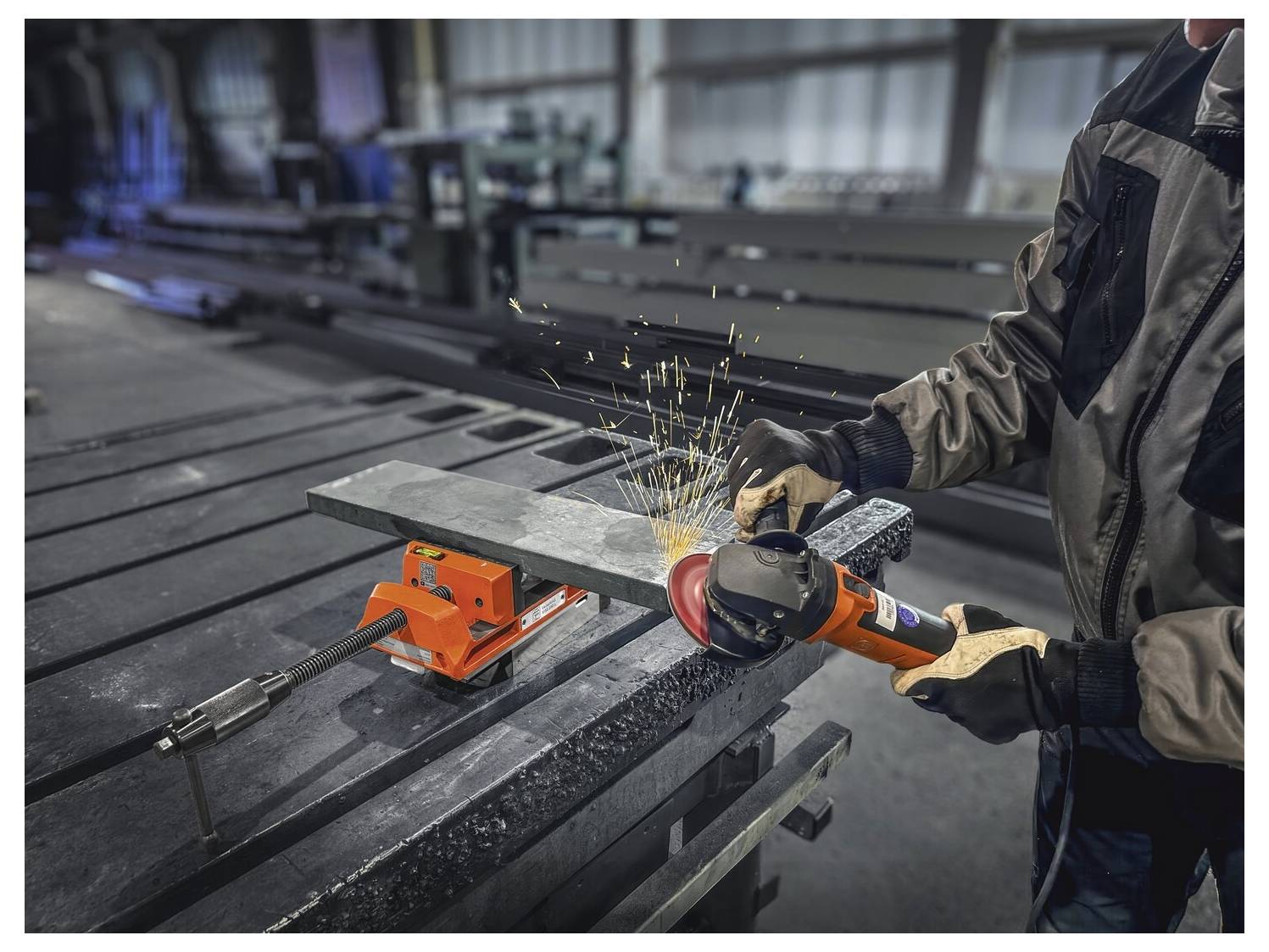 Eine Person benutzt einen tragbaren Schleifer, um einen Metallstab zu schneiden, der in einer Werkbank eingespannt ist, wobei Funken in einer Industriewerkstatt-Umgebung fliegen.