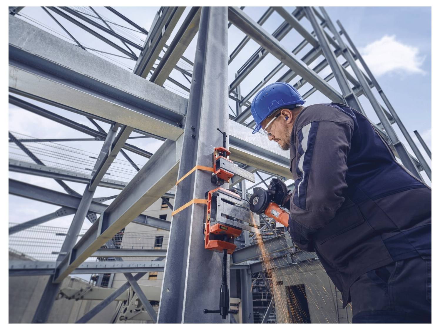 Ein Bauarbeiter in einem blauen Helm verwendet Elektrowerkzeuge, um einen Stahlträger in einem Gebäuderahmen zu schneiden, wobei Funken fliegen.