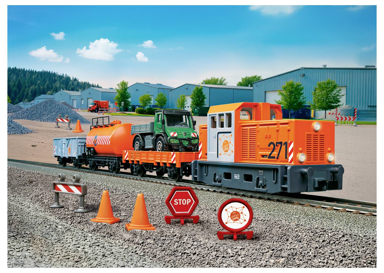 Ein Spielzeugzug mit einer orangefarbenen Lokomotive, einem Güterwagen mit Fahrzeug und einem Kesselwagen auf einem Gleis. Kegel, Stoppschild und Steine in der Nähe.