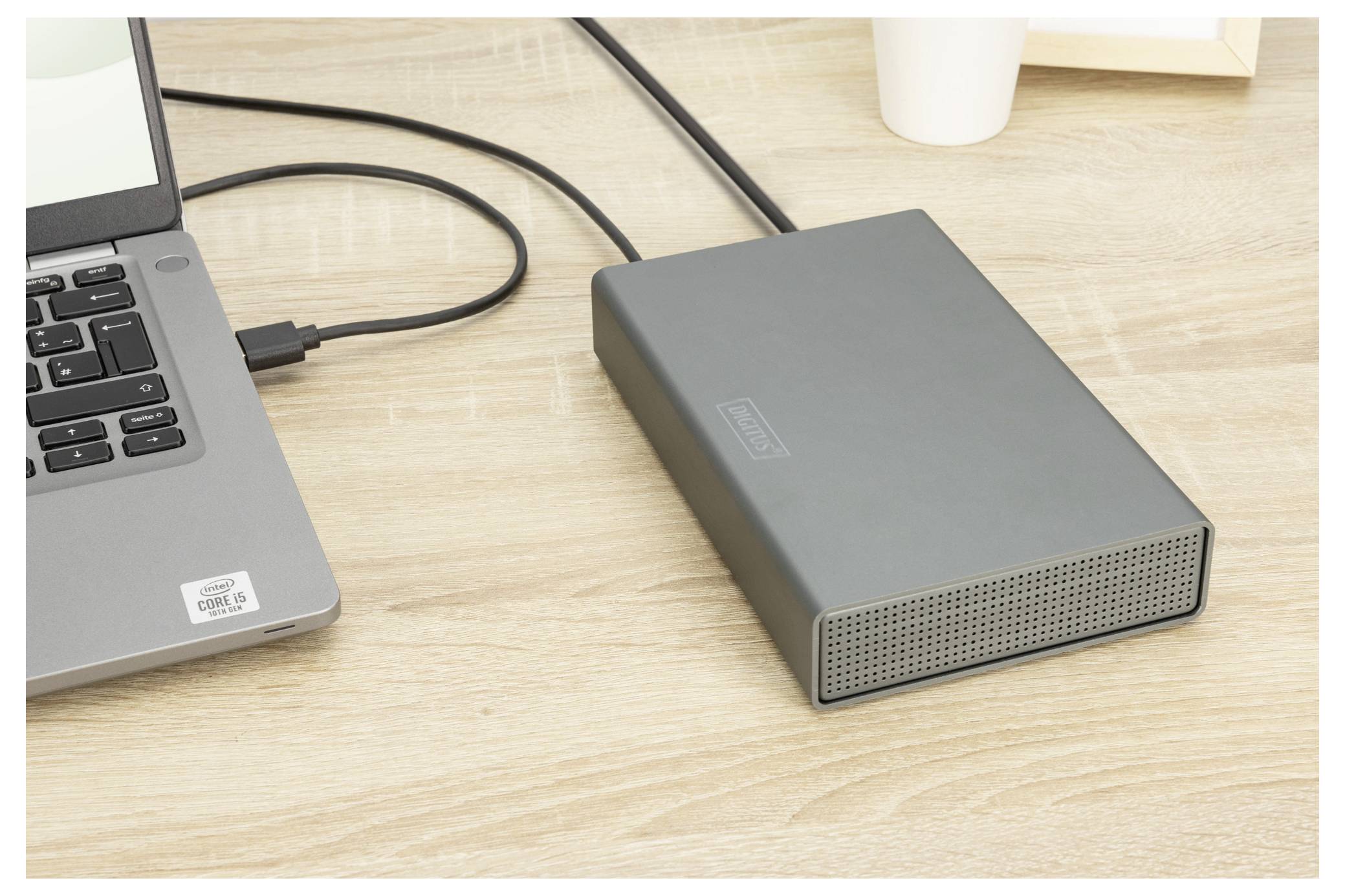 Ein Laptop ist mit einer externen Festplatte auf einem Holzschreibtisch verbunden, was auf eine Datenübertragung oder Sicherungsaktivität hindeutet.