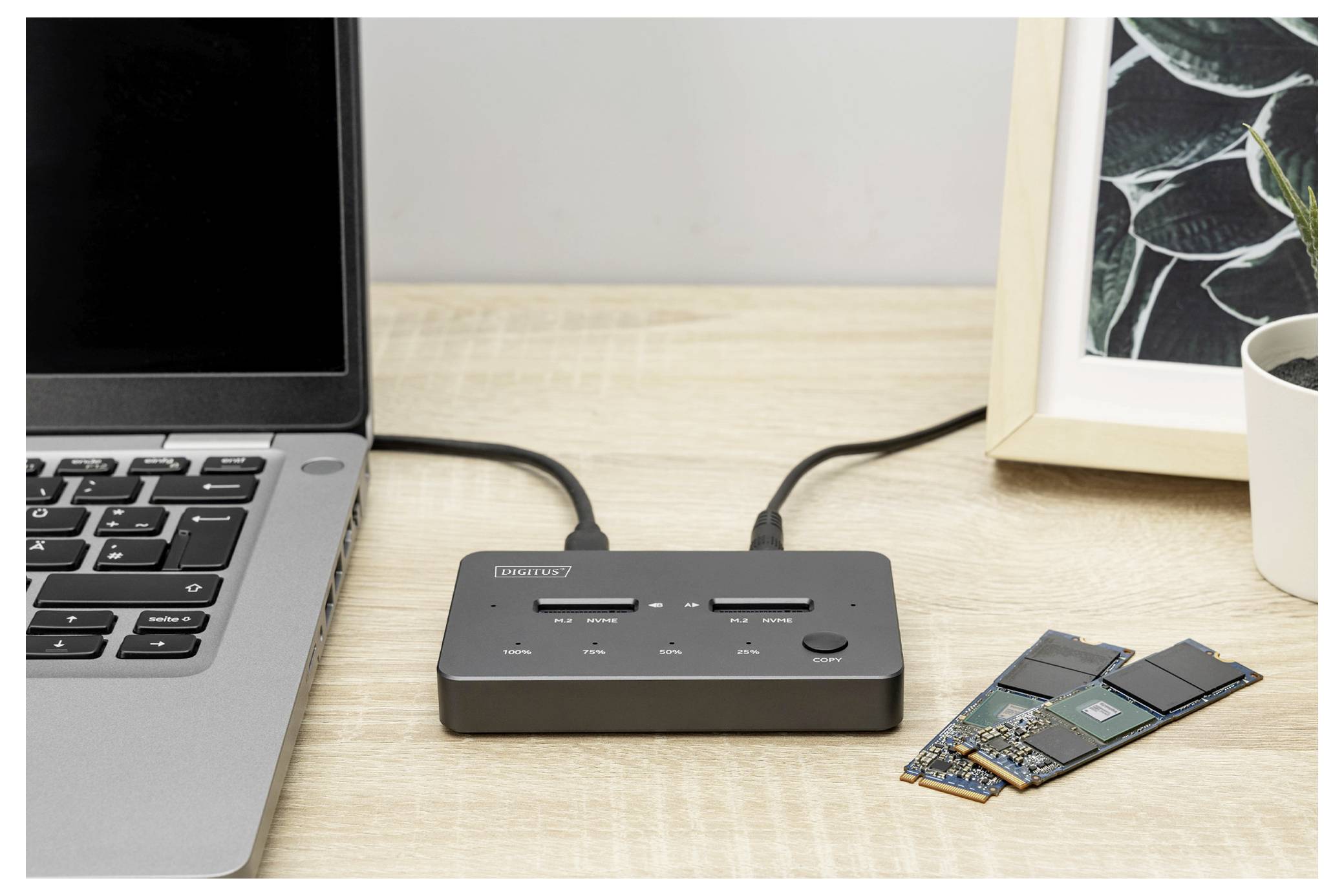 Ein USB-Hub mit mehreren Anschlüssen ist an einem Holzschreibtisch mit einem Laptop verbunden. Zwei M.2-Laufwerke sind neben dem Hub platziert.