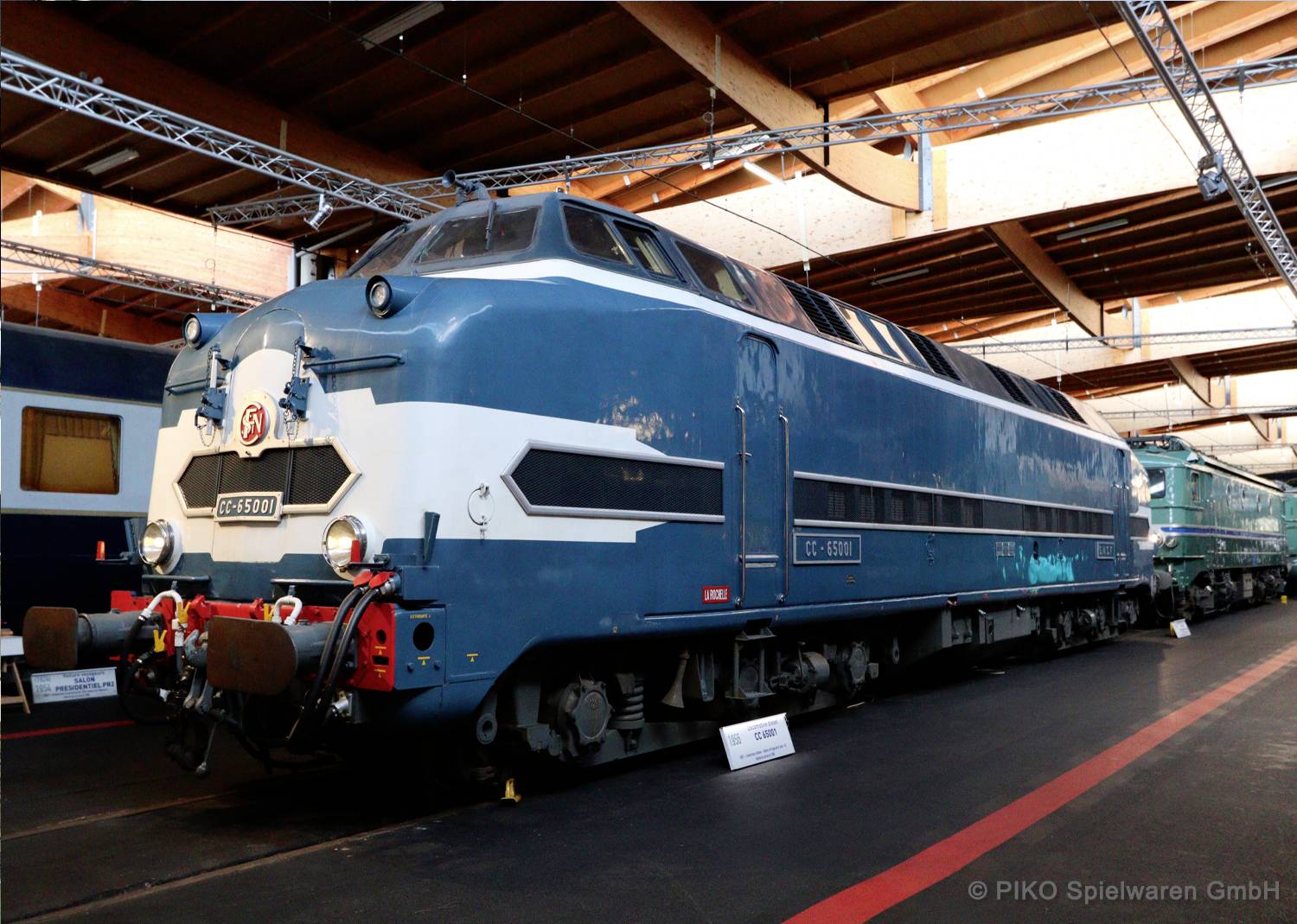 Eine blaue Vintage-Lokomotive, die in einem Innenraum auf Gleisen ausgestellt ist, mit der Beschriftung 