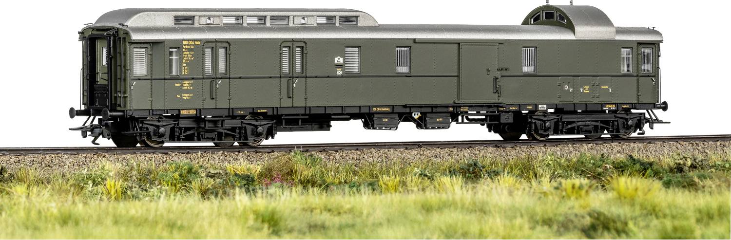 Ein grüner Vintage-Eisenbahnwagen auf Bahngleisen, mit detailliertem Metallwerk und kleinen Fenstern, vor einem verschwommenen Vordergrund mit Gras.