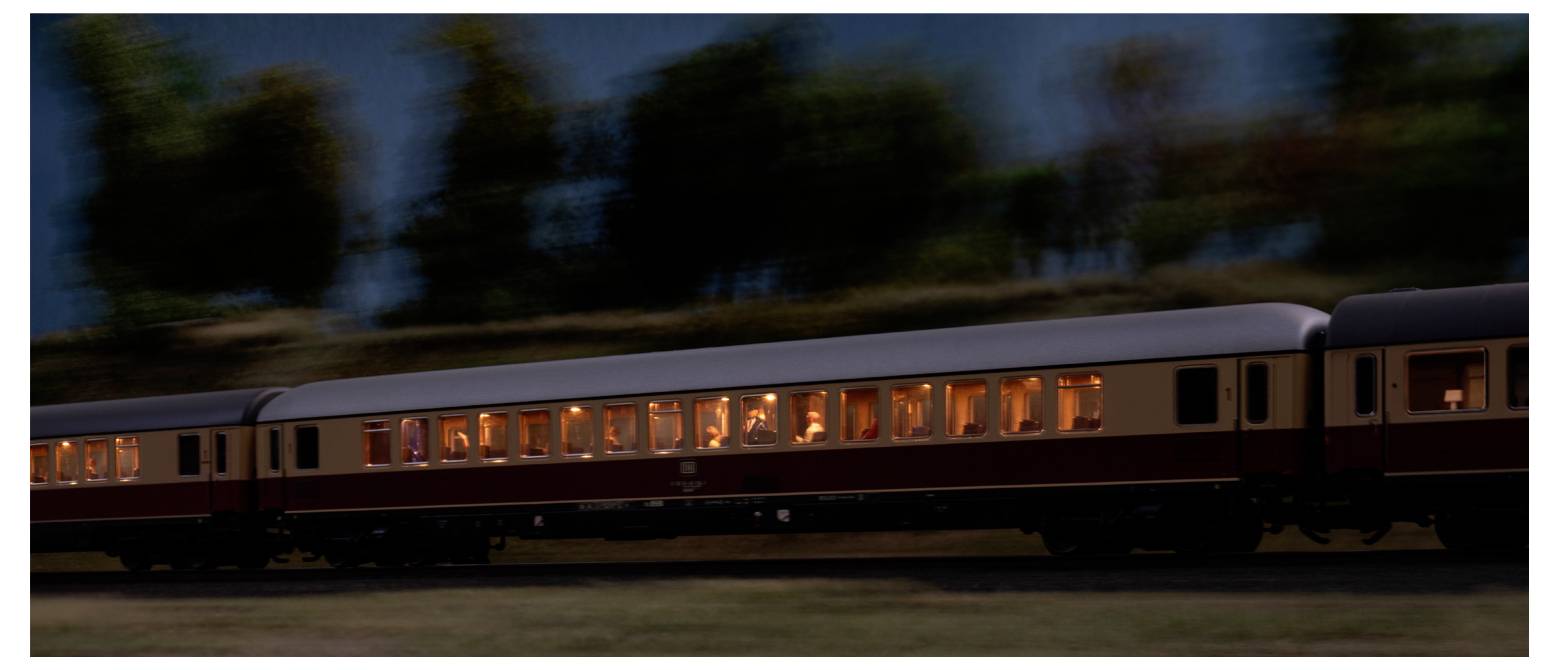 Ein Zug mit schwach beleuchteten Fenstern fährt nachts durch eine Landschaft mit verschwommenen Bäumen, was Bewegung und Geschwindigkeit andeutet.