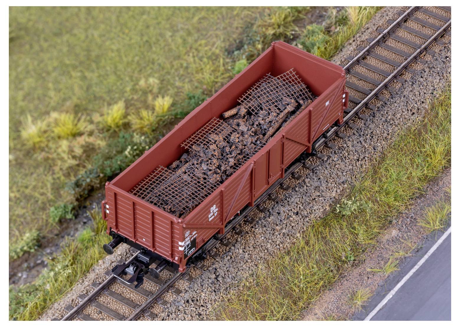Ein Modelleisenbahn-Güterwagen gefüllt mit Kohlebrocken fährt auf Miniaturschienen, umgeben von Gras und präsentiert eine detaillierte Eisenbahnszene.