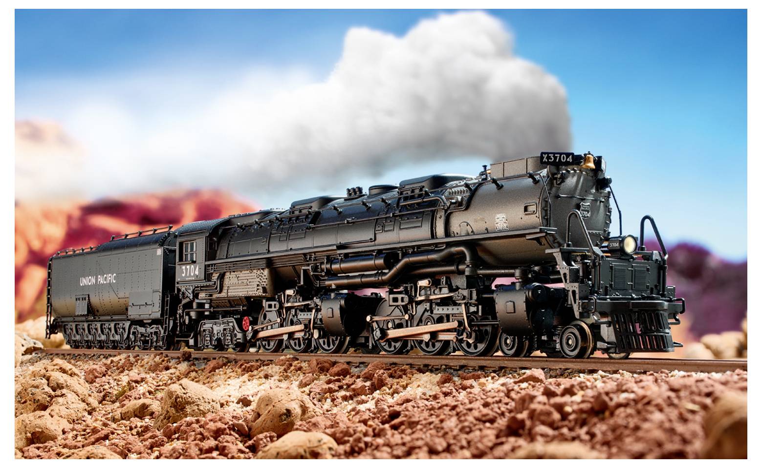 Ein Modellzug-Güterwagen sitzt auf den Gleisen und trägt zwei schwarze Radaufhängungen. Die umgebende Szenerie umfasst Gras und Kies.