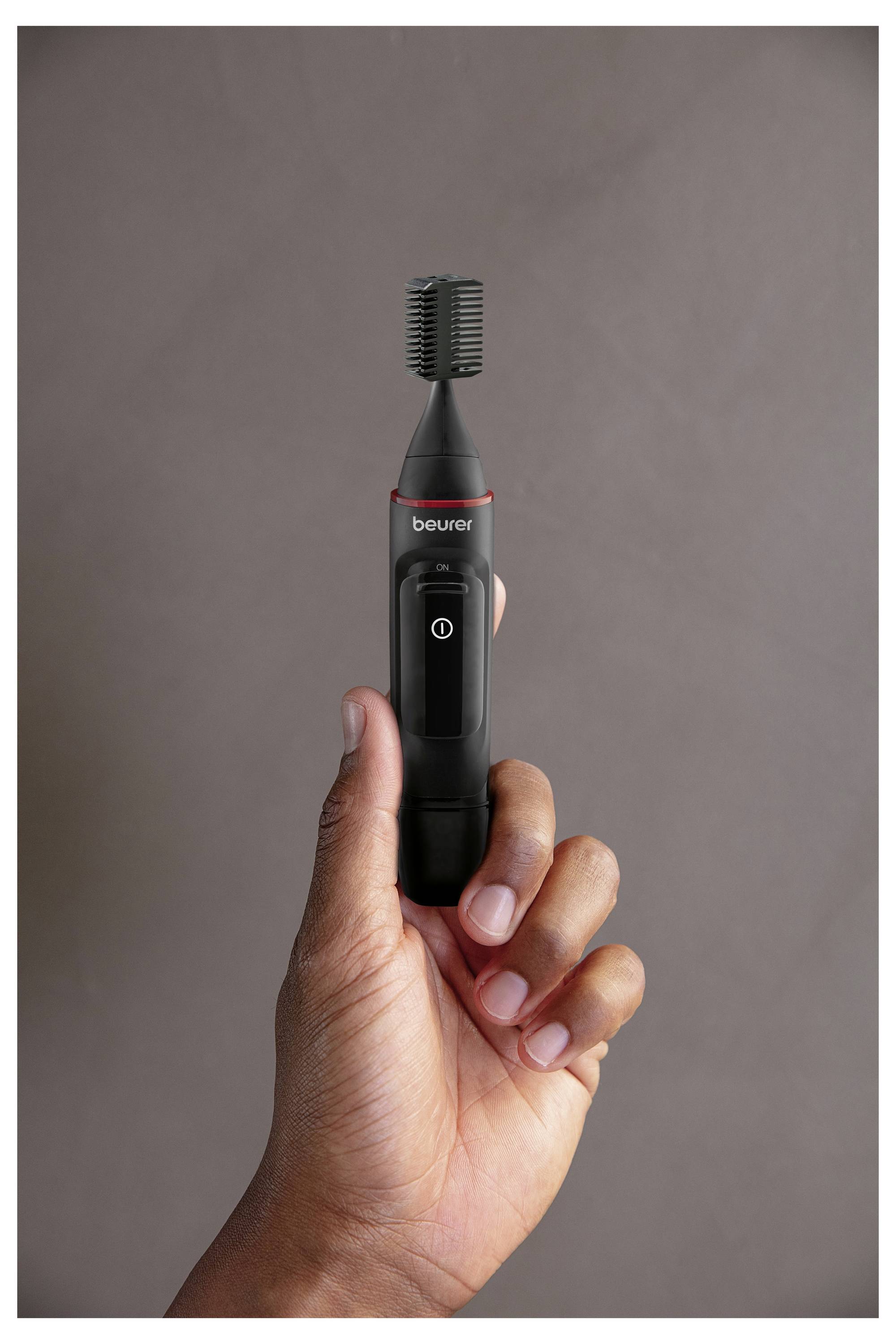 Eine Hand, die ein schwarzes Grooming-Werkzeug mit rundem Bürstenkopf und Ein-/Aus-Schalter hält, vor einem einfachen Hintergrund.