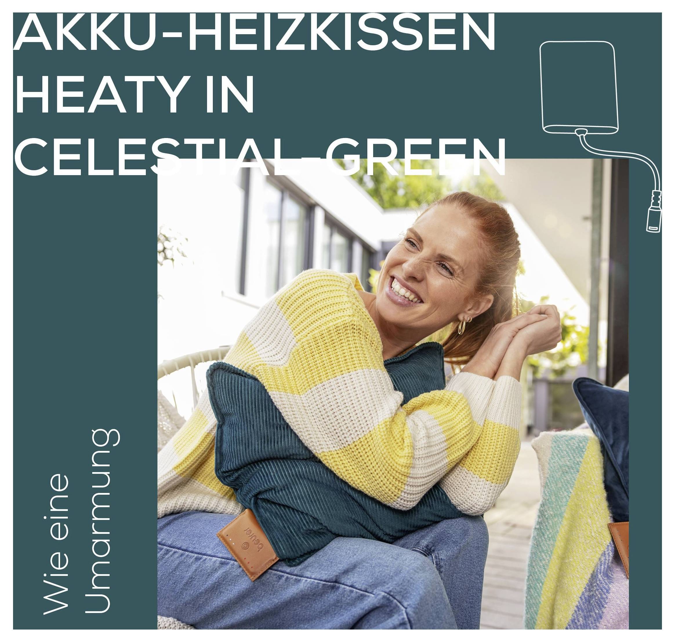 Frau sitzt in einem gemütlichen Sessel und umarmt ein Kissen. Der Text lautet: Akku-Heizkissen Heaty in Celestial Green, Wie eine Umarmung.