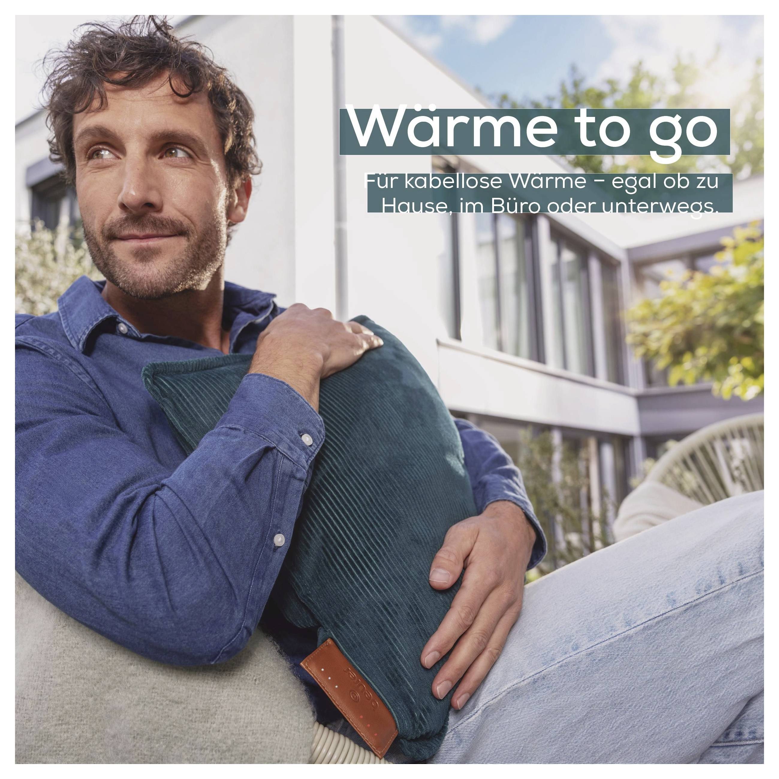 Ein Mann sitzt im Freien mit einem türkisfarbenen Kissen. Der Text auf Deutsch lautet „Wärme to go