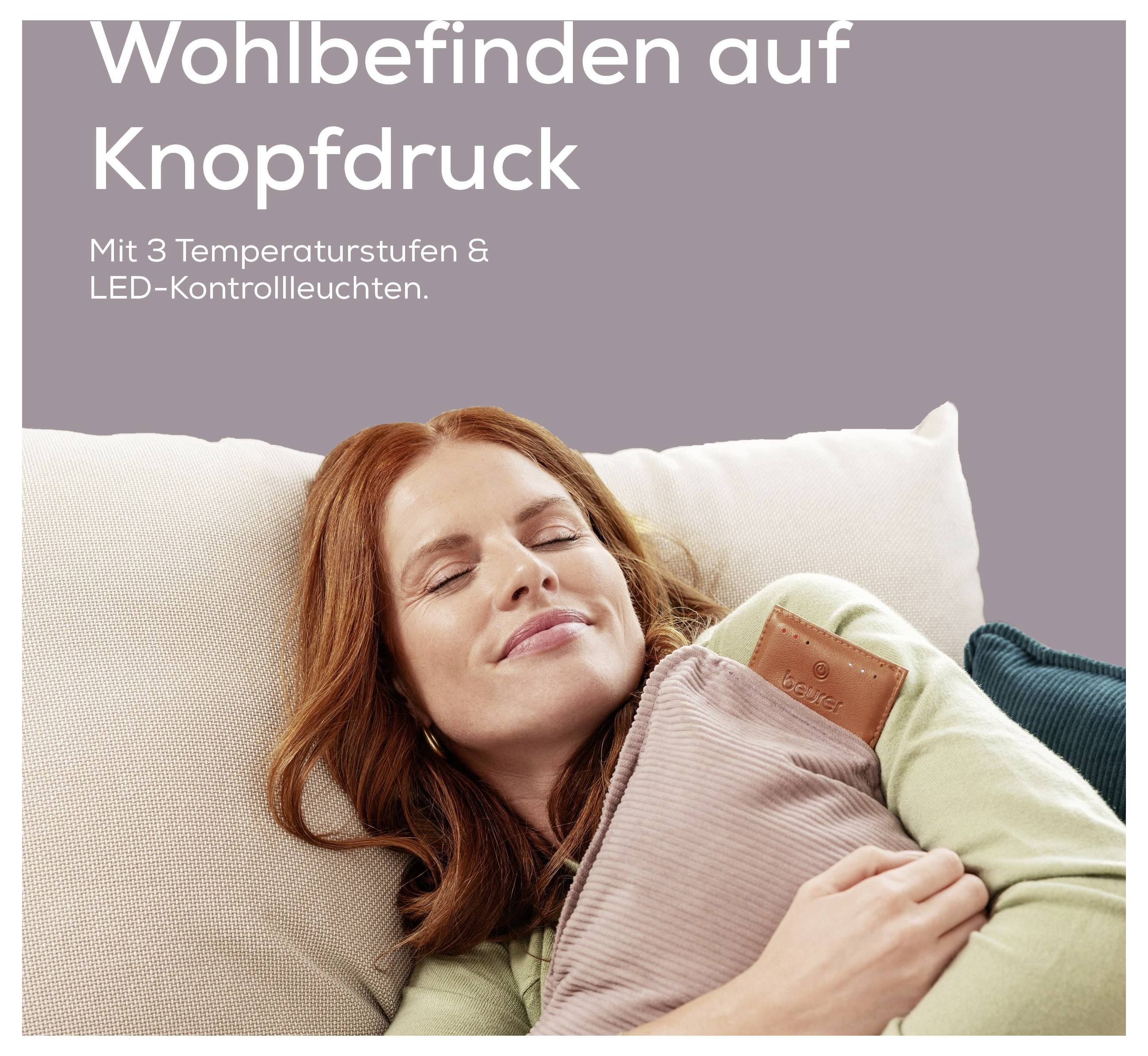 Eine Frau entspannt sich auf einem Sofa und hält ein Wärmekissen. Der Text lautet: „Wohlbefinden auf Knopfdruck. Mit 3 Temperaturstufen & LED-Kontrollleuchten.