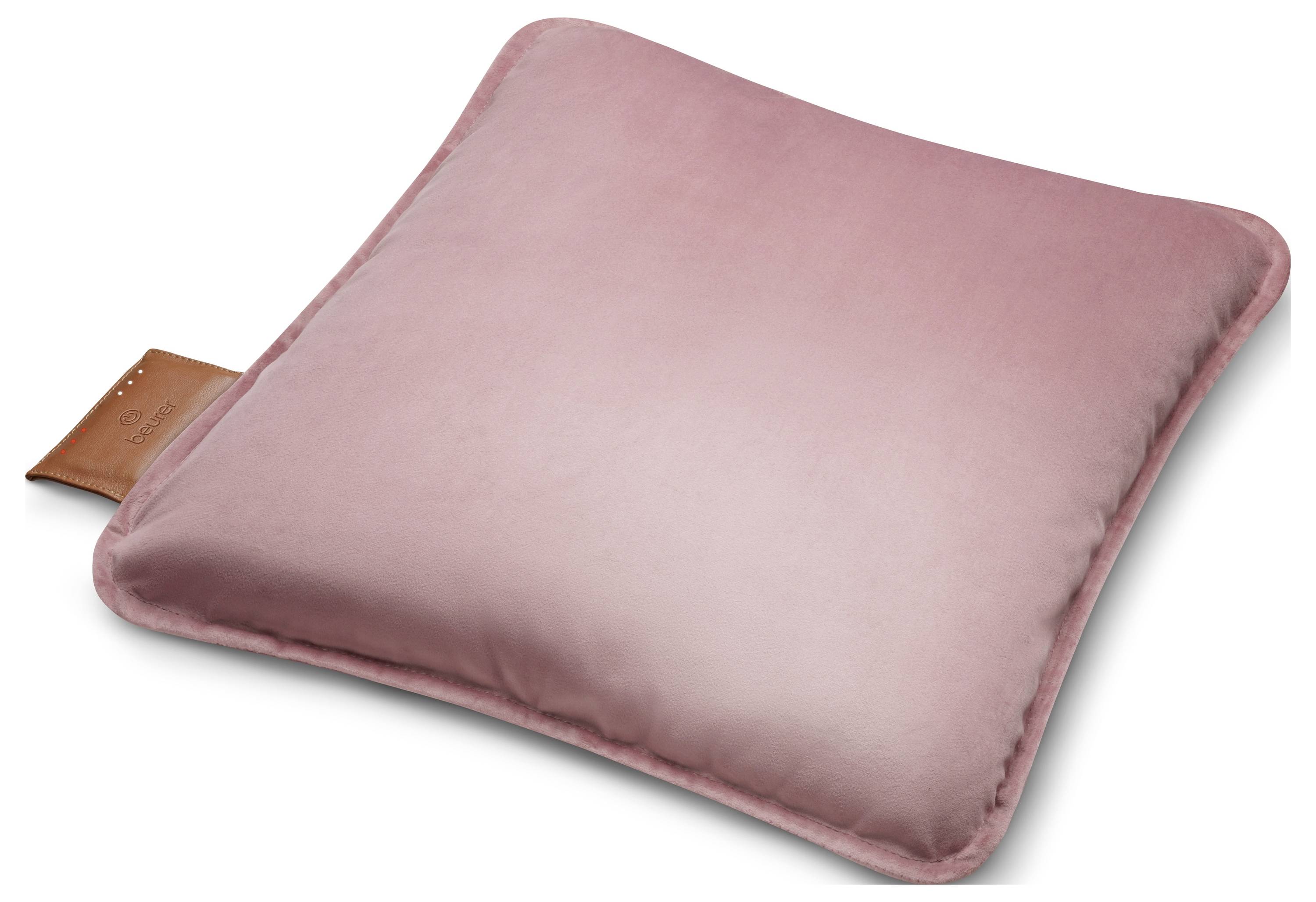 Ein quadratisches, weiches rosa Kissen mit einem Lederanhänger an einer Kante, vor einem einfachen Hintergrund.