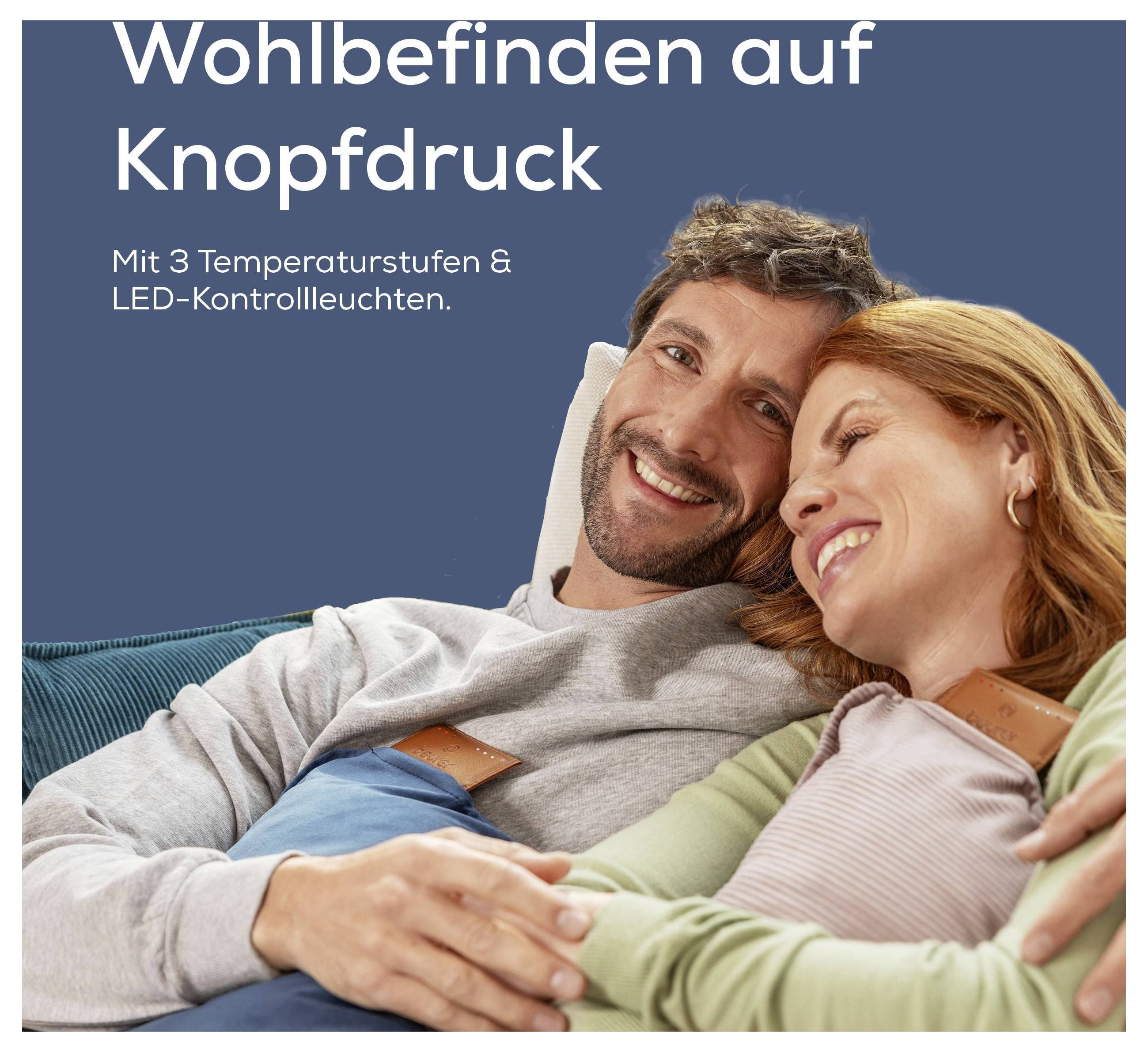 Ein Mann und eine Frau lächeln, lehnen sich zurück und nutzen ein elektrisches Wärmekissen. Der Text sagt: 