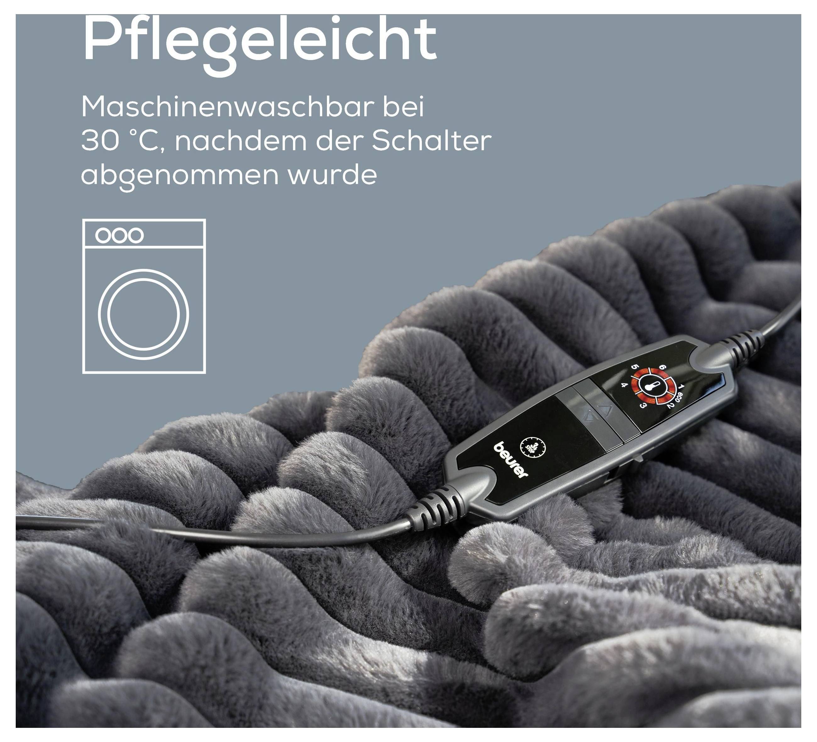 Eine weiche, graue Decke mit einem Bediengerät ruht darauf. Der Text in deutscher Sprache hebt maschinenwaschbare Eigenschaften bei 30 °C hervor.