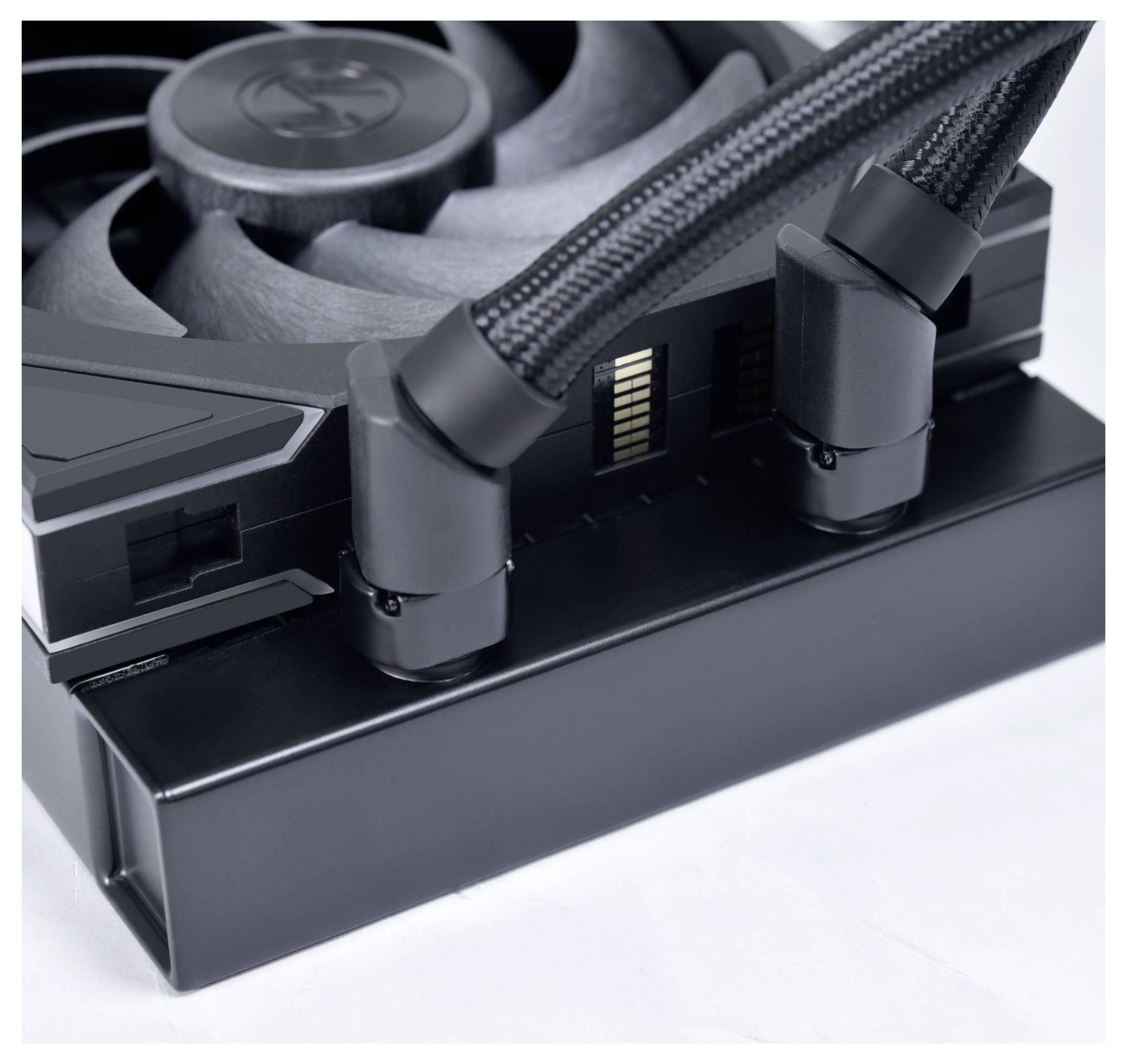 Eine Nahaufnahme eines Computerkühlers zeigt einen Lüfter und zwei geflochtene Schläuche, die mit einem schwarzen Kühler verbunden sind.