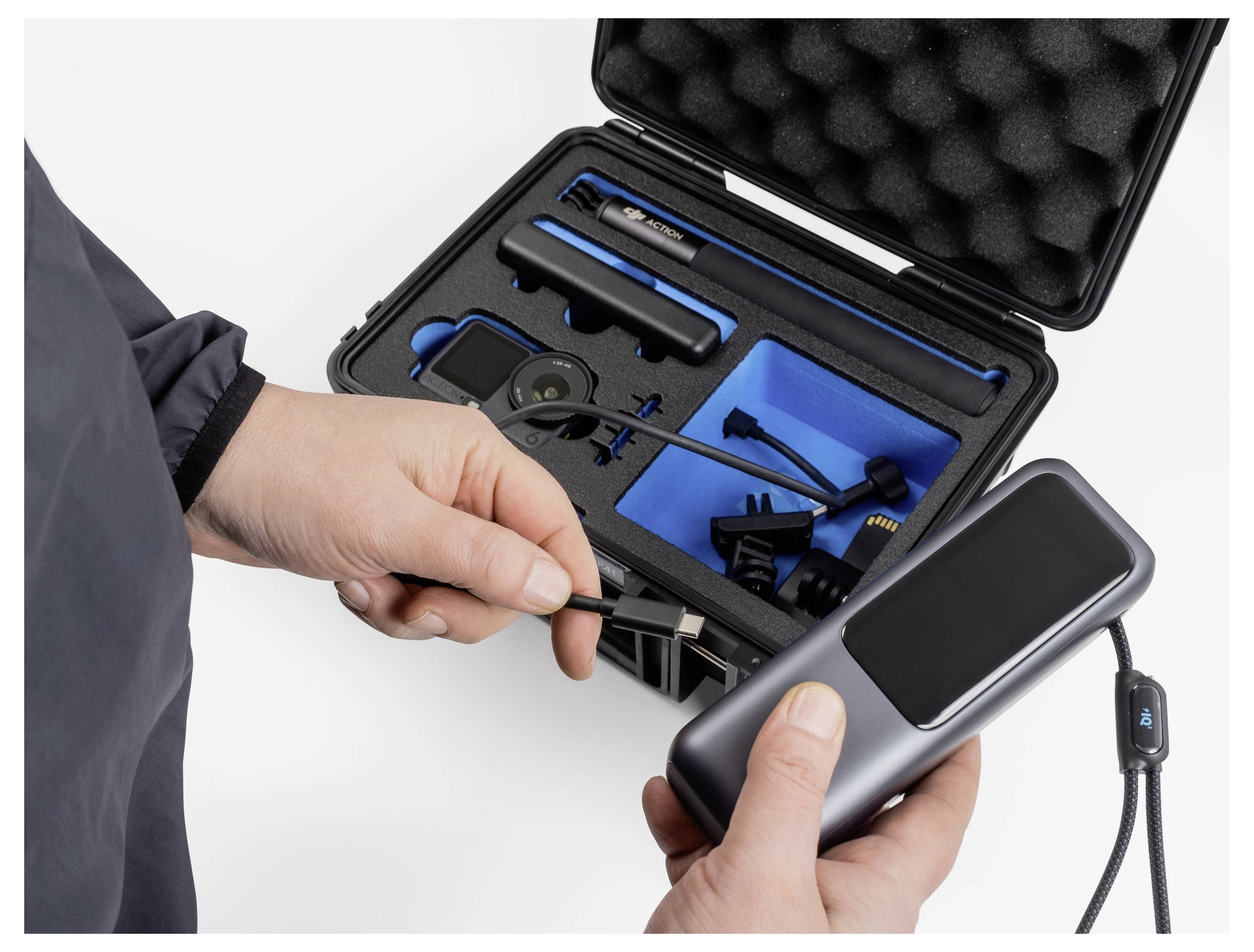 Person, die ein tragbares elektronisches Gerät hält und sich darauf vorbereitet, es mit Komponenten in einem offenen, schaumstoffausgekleideten Schutzkoffer zu verbinden.