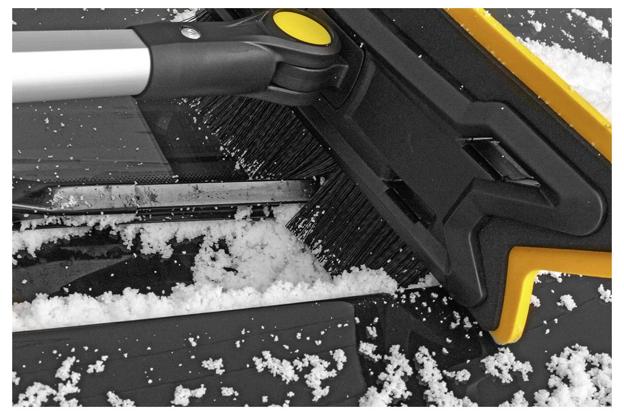 Eine Schneeebürste mit schwarzem Borsten­kopf und gelben Details räumt Schnee von einer Autoscheibe.