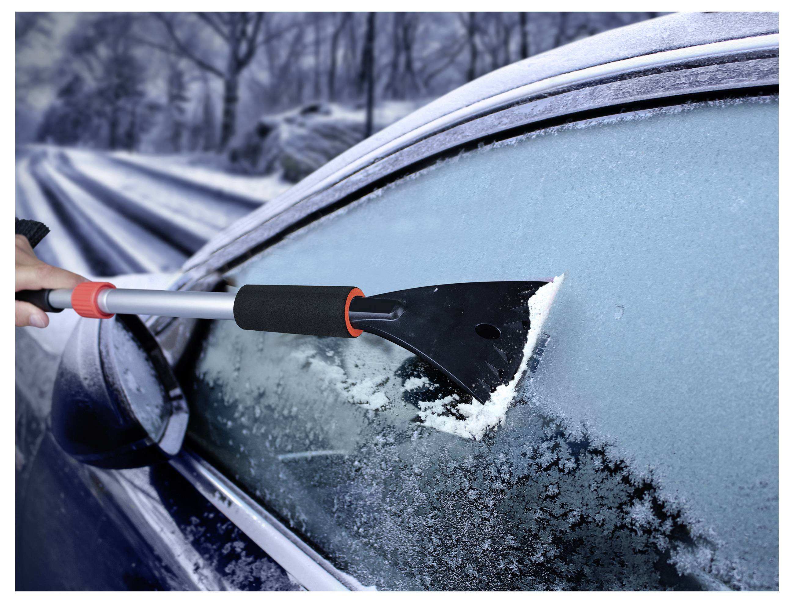 Die Hand einer Person verwendet einen schwarzroten Eiskratzer, um Eis von der Seitenscheibe eines Autos am schneebedeckten Straßenrand zu entfernen.