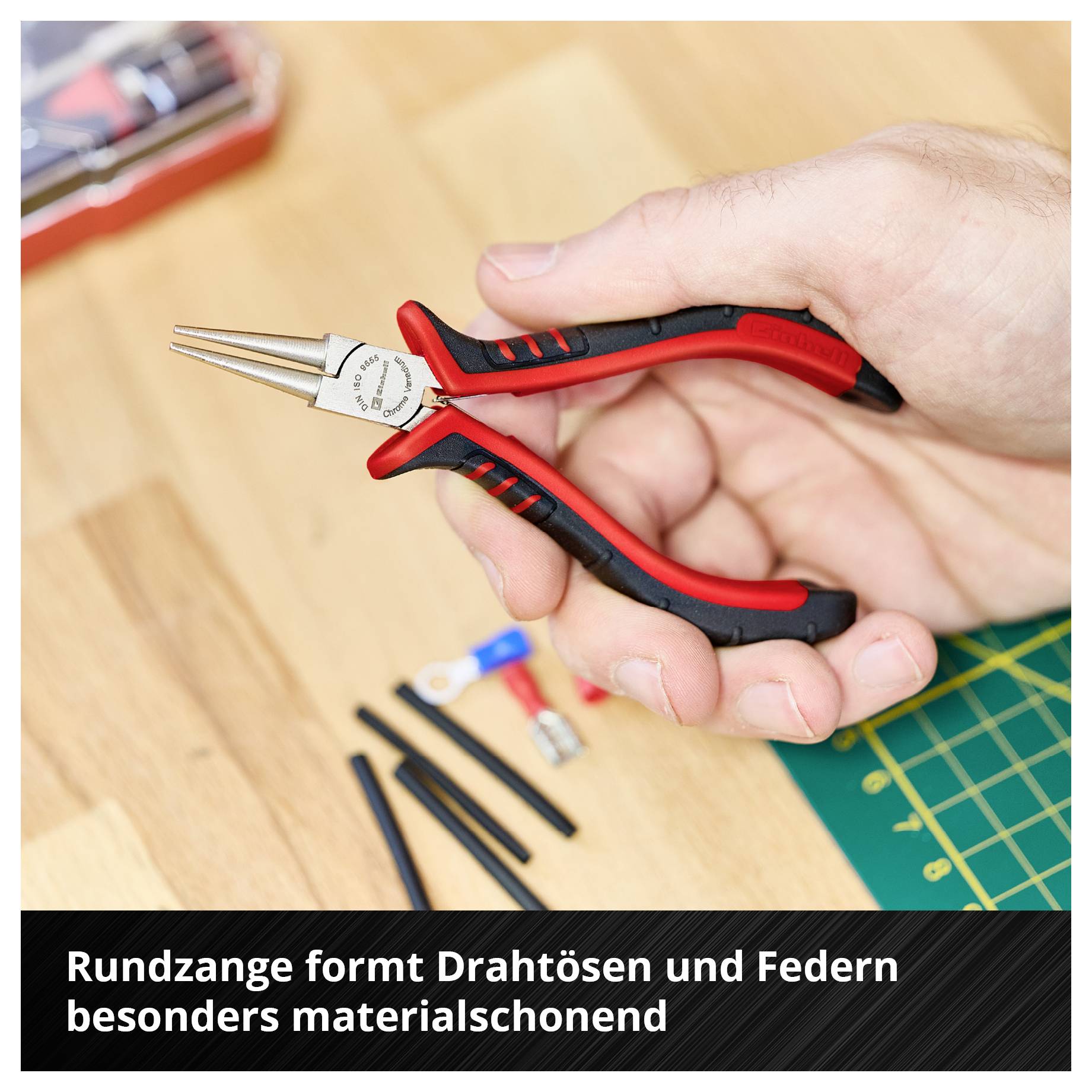 Hand hält eine schwarze und rote Rundzange über einem Tisch mit kleinen Metallteilen und Werkzeug. Text unten: 'Rundzange formt Drahtösen und Federn besonders materialschonend'.