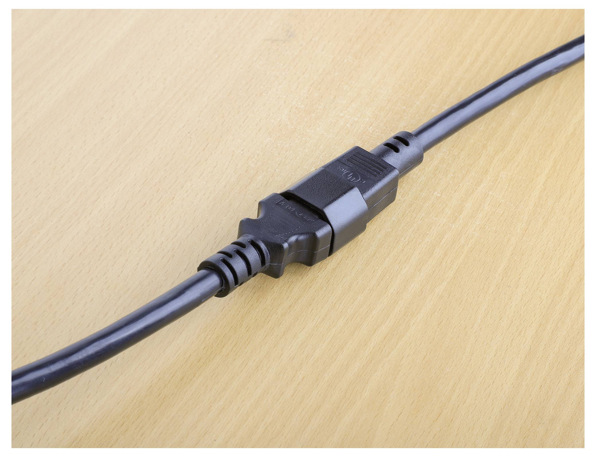 Ein schwarzes Stromkabel mit zwei zusammengefügten Steckern, auf einer hellen Holzoberfläche platziert.