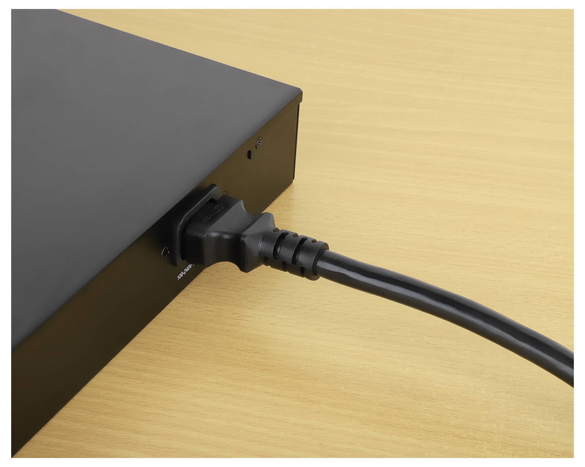 Ein schwarzes Stromkabel ist in ein elektronisches Gerät auf einer Holzoberfläche eingesteckt, was darauf hindeutet, dass es eingeschaltet ist oder in Benutzung ist.