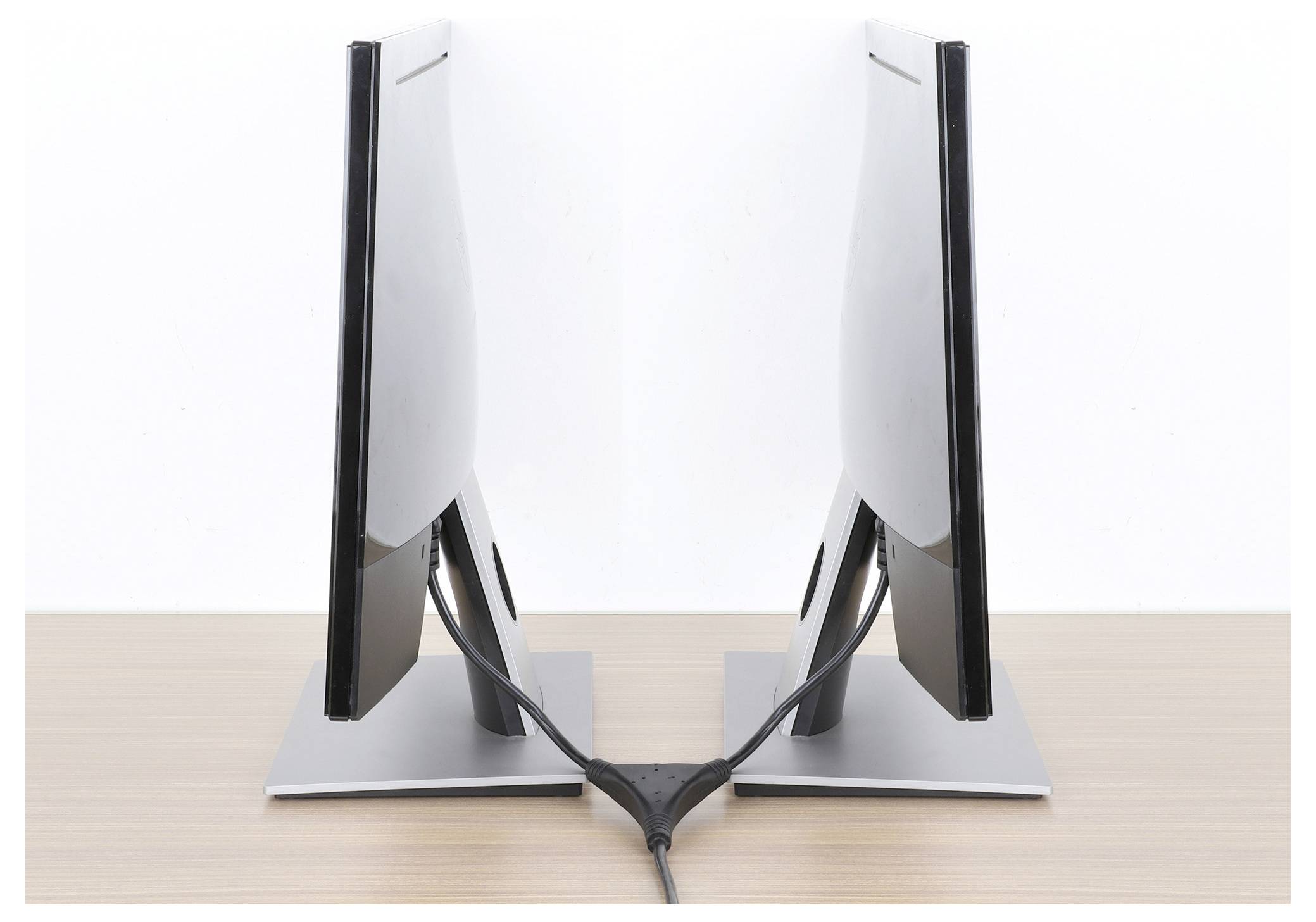 Zwei moderne Flachbildschirme, die sich auf einer Holzoberfläche rückling gegenüber stellen, mit Kabeln, die am unteren Ende verbunden sind.