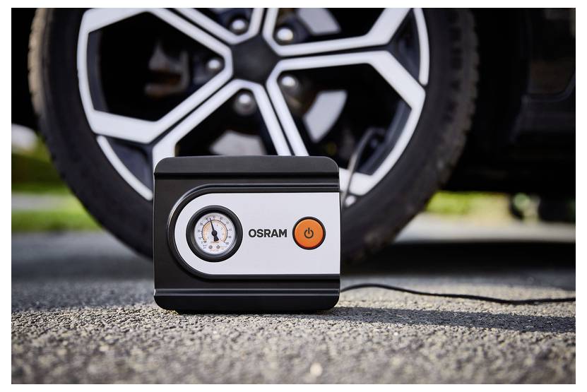 Ein Reifenaufblasgerät der Marke 'Osram' steht auf dem Boden vor einem Autoreifen und zeigt ein Druckmessgerät und einen Stromschalter an.