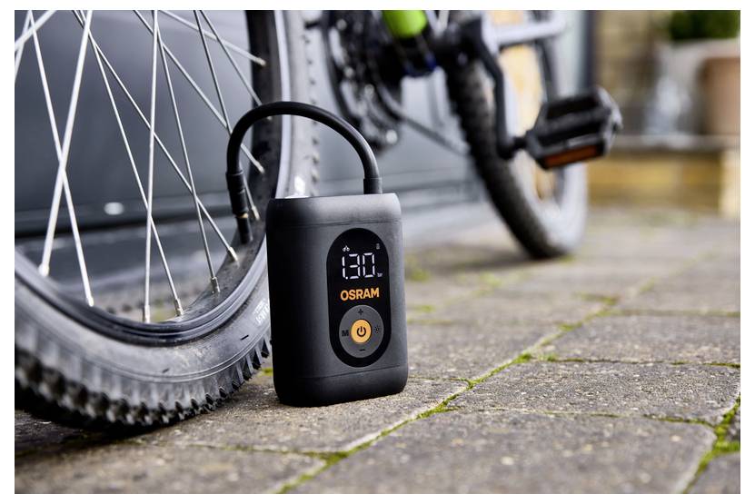 Ein tragbarer Luftkompressor befüllt einen Fahrradreifen. Das digitale Display des Kompressors zeigt „13.0