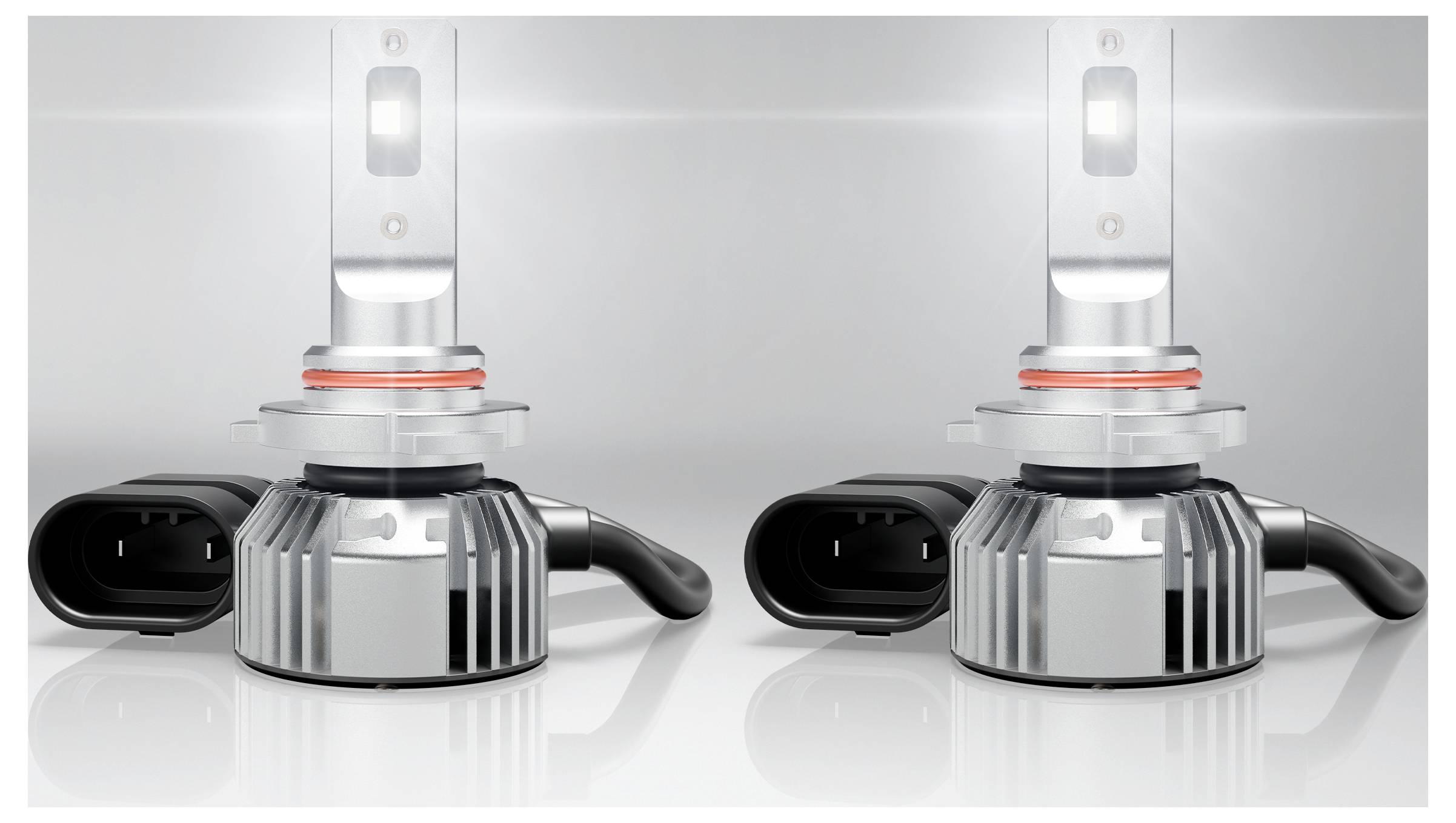 Zwei LED-Scheinwerferleuchtmittel mit Kühlrippen und Stromsteckverbindern, gegen einen reflektierenden Hintergrund positioniert, die weiches Licht ausstrahlen.