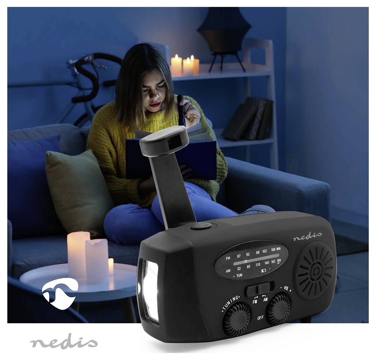 Eine Person sitzt auf einem Sofa und liest ein Buch beim Kerzenlicht. Im Vordergrund wird ein Nedis-Radio mit Taschenlampe und manueller Handkurbel ausgestellt.