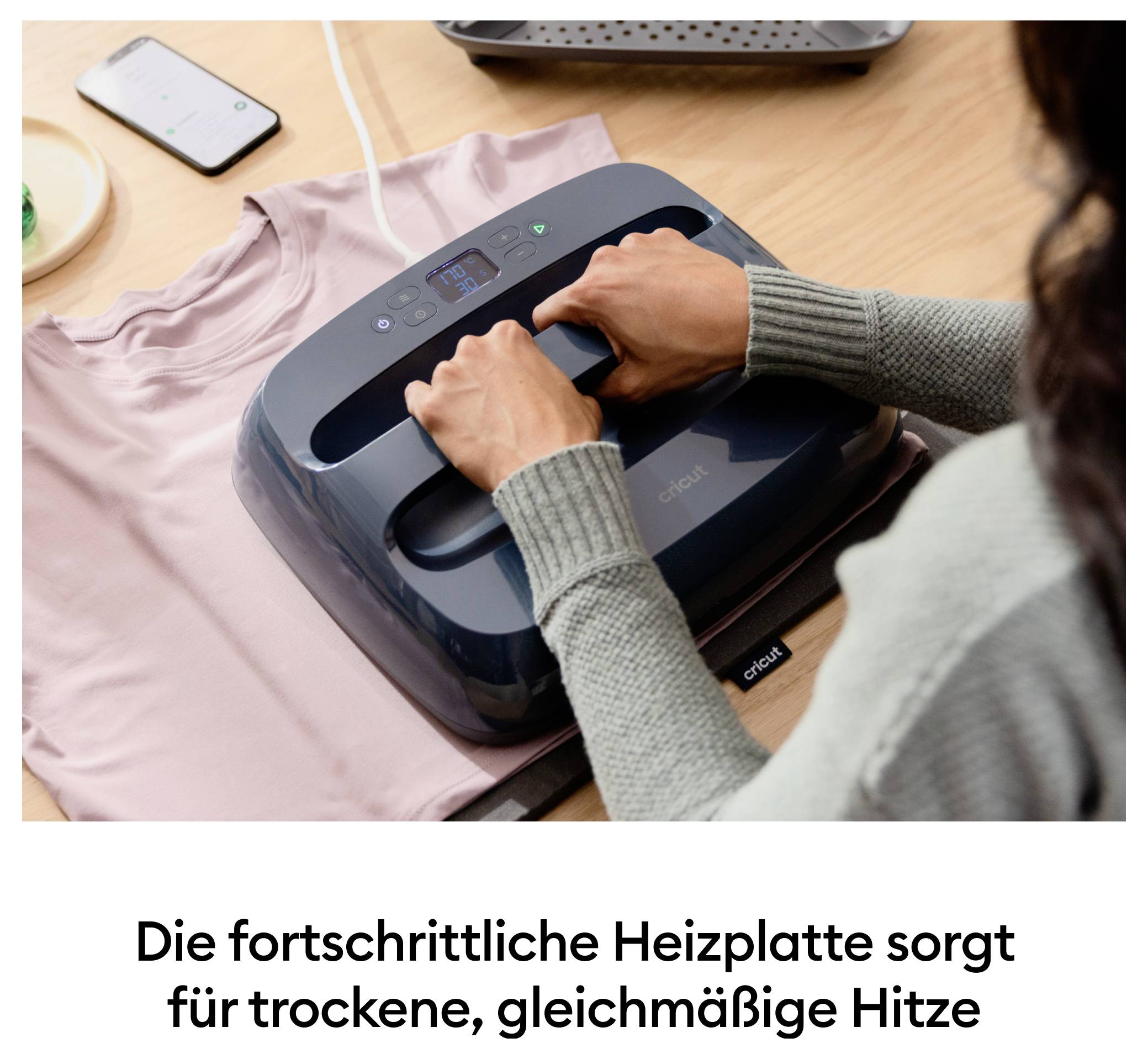 Eine Person bedient eine moderne Heizplatte, um ein T-Shirt gleichmäßig zu erhitzen. Die Anzeige auf dem Gerät ist aktiviert.