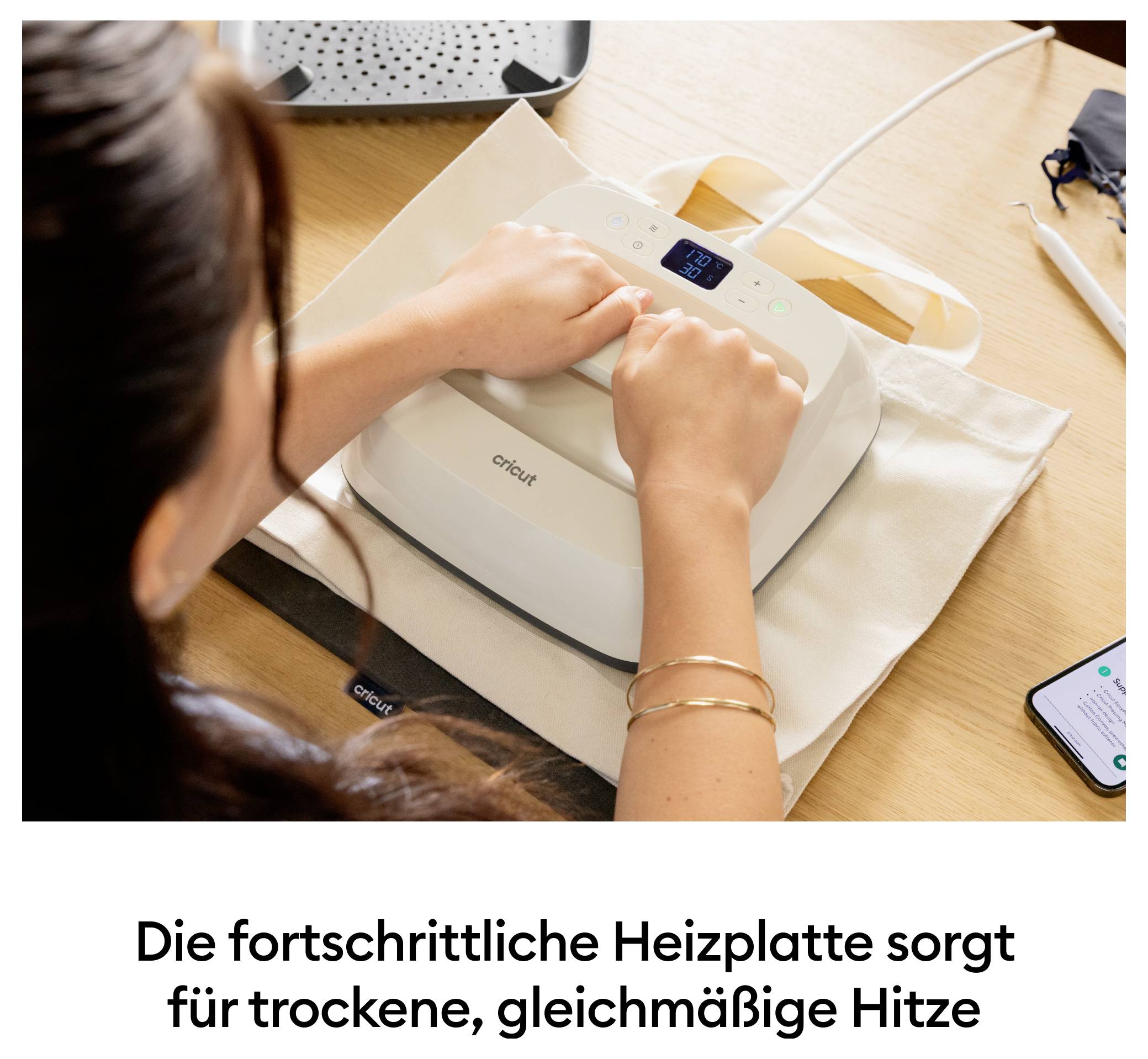 Eine Person bedient eine weiße Heizpresse auf einem Stoffbeutel. Text unten: 'Die fortschrittliche Heizplatte sorgt für trockene, gleichmäßige Hitze'.