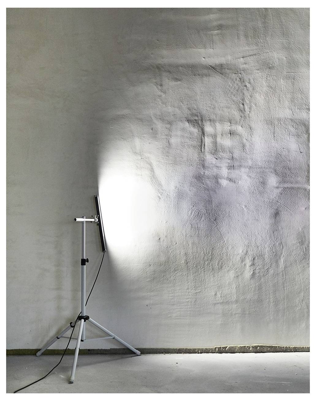 Eine Stehlampe beleuchtet eine strukturierte weiße Wand in einem minimalistischen Raum und hebt dabei die raue Oberfläche und subtile Schatten hervor.