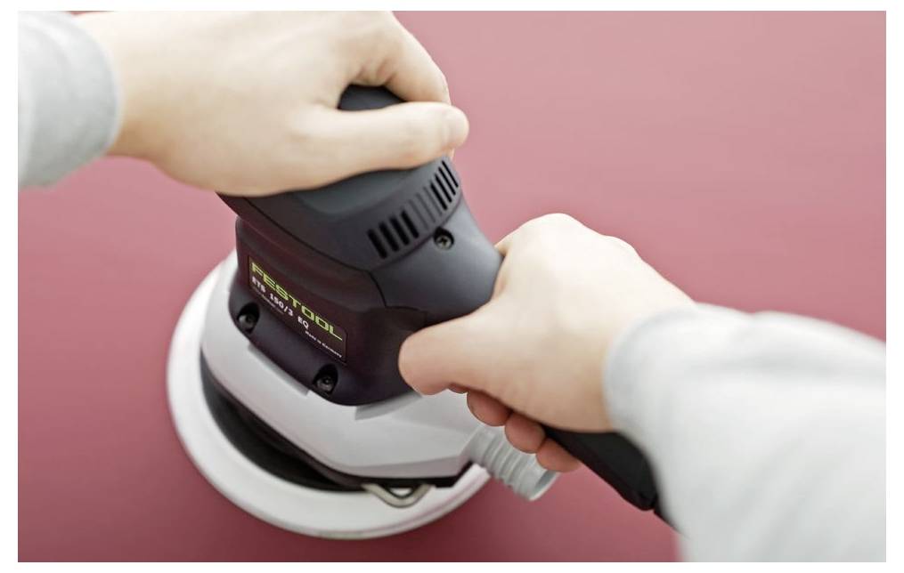 „Hände, die einen elektrischen Schleifschwamm auf einer glatten roten Oberfläche verwenden, zeigen eine Draufsicht des Werkzeugs in Betrieb.