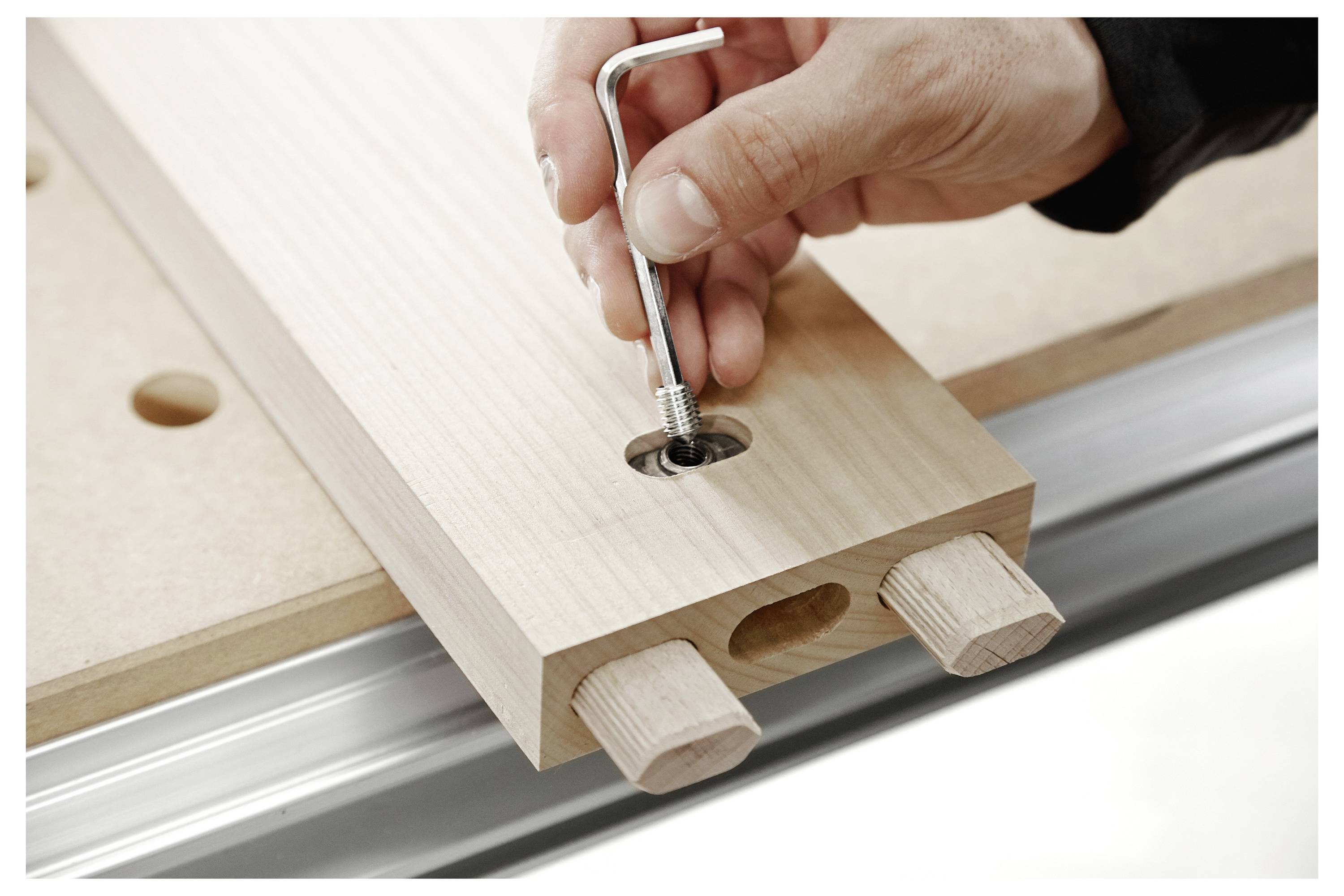 Eine Hand benutzt einen Inbusschlüssel, um eine Schraube an einer Holzverbindung einzustellen und zeigt die Holzbearbeitung zusammen mit Präzisionswerkzeugen.