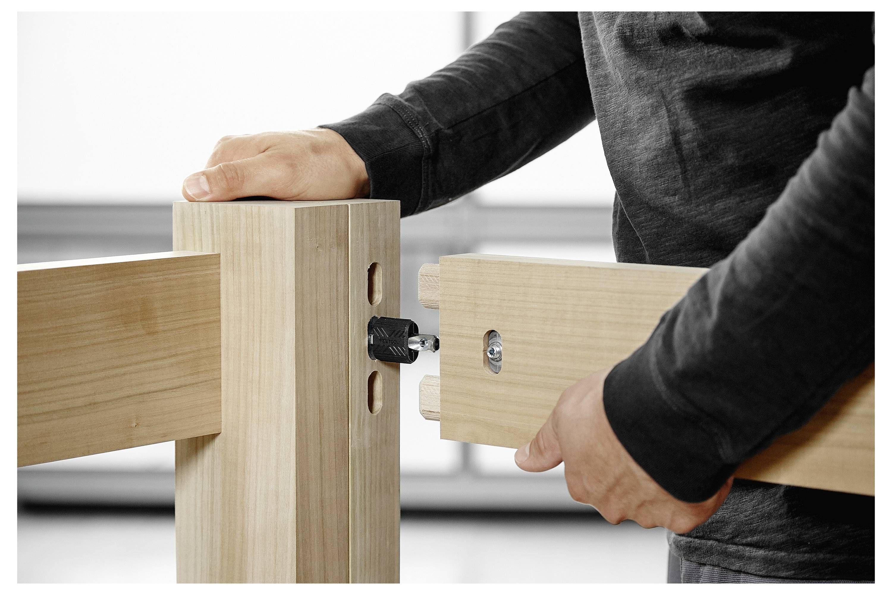 Nahaufnahme von zwei Holzpaneelen, die in einem rechten Winkel mit Metallverbindern verbunden werden, was die Montagetechnik auf einer Tischoberfläche demonstriert.