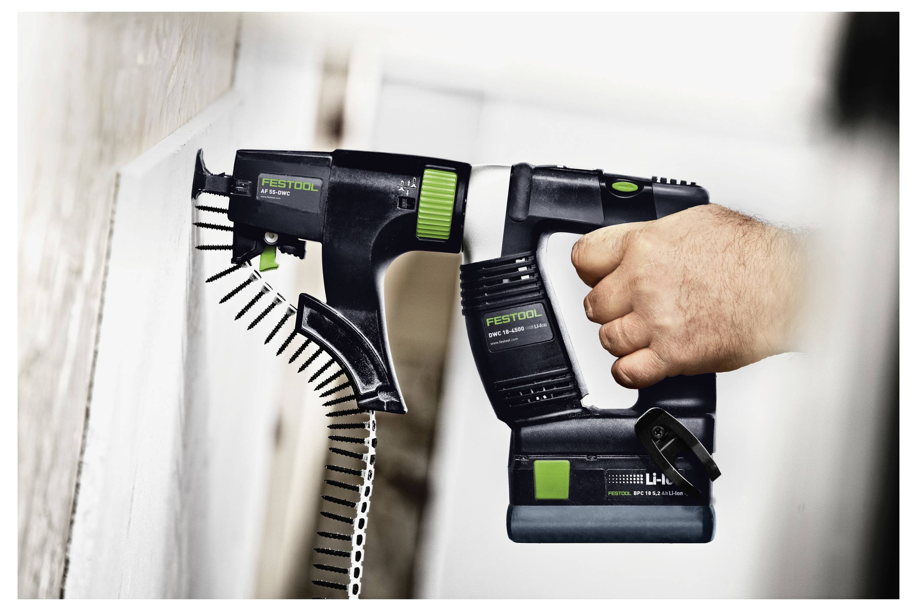 Eine Person benutzt einen Festool-Trockenbauschaber, um Schrauben in eine Wand zu treiben. Das Werkzeug ist kompakt mit grünen Akzenten und einer Schraubenschleifer-Befestigung.